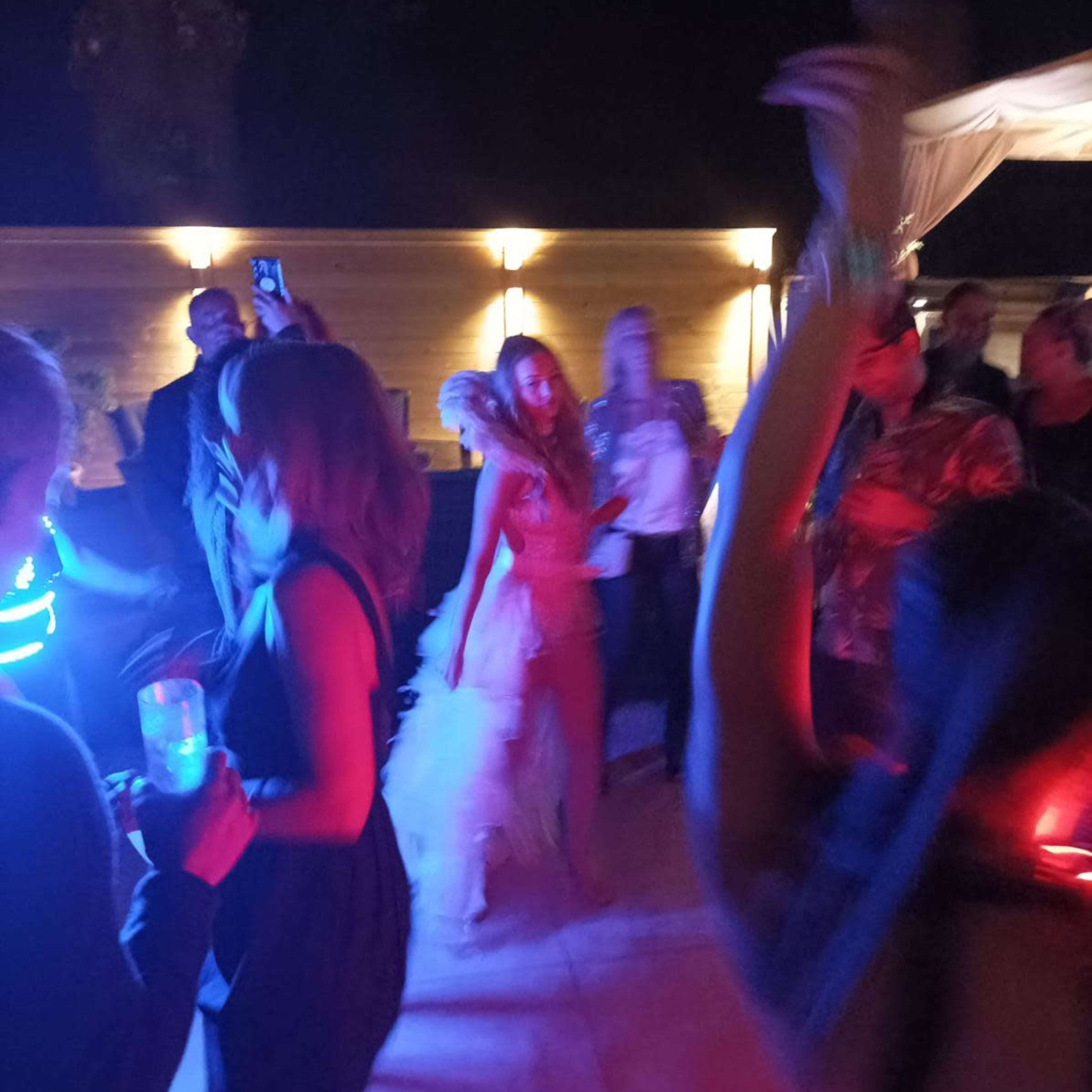 A group of people dances at a nighttime outdoor party with colorful lights illuminating the scene.