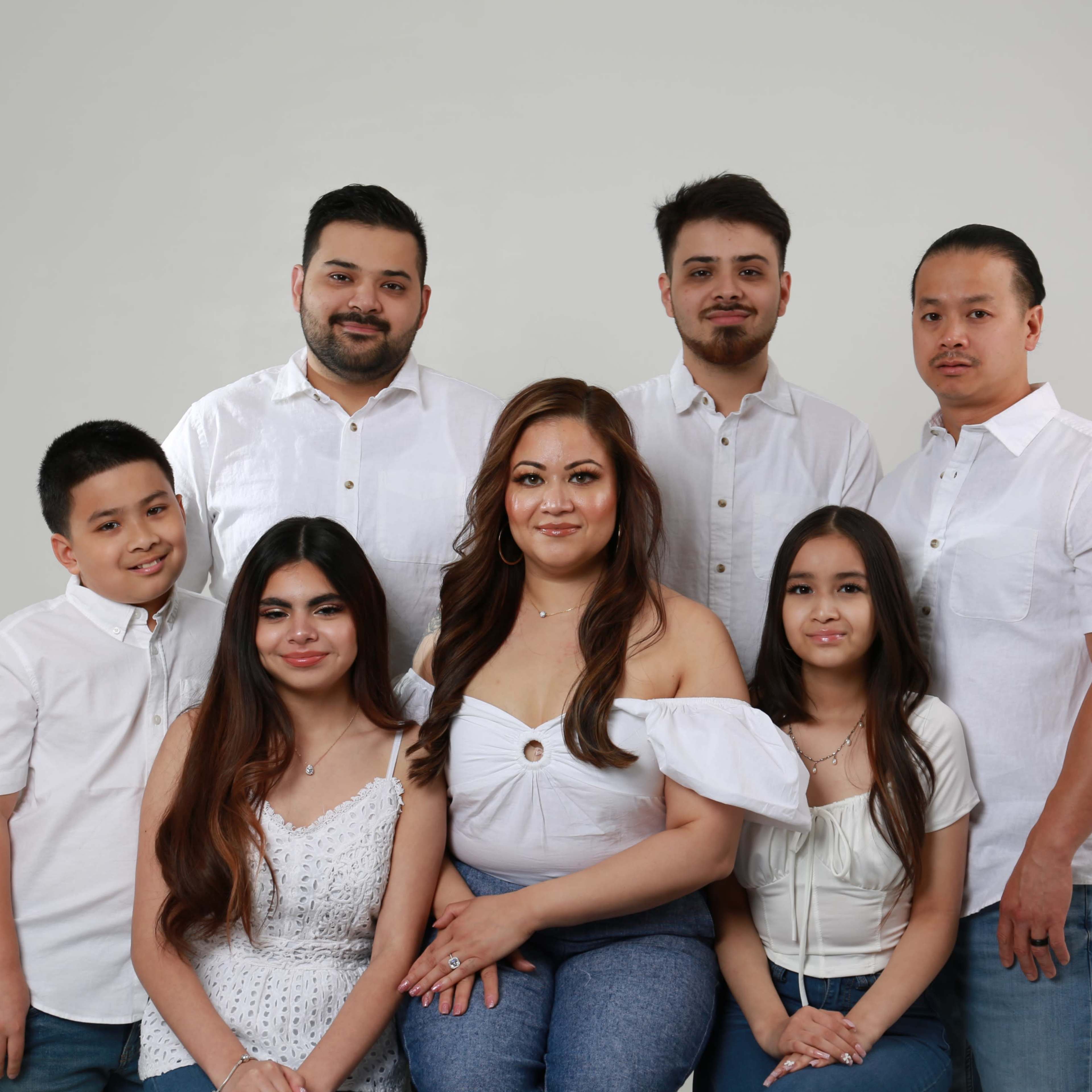 A group of seven individuals wearing white shirts and blue jeans poses together in front of a light-colored backdrop.