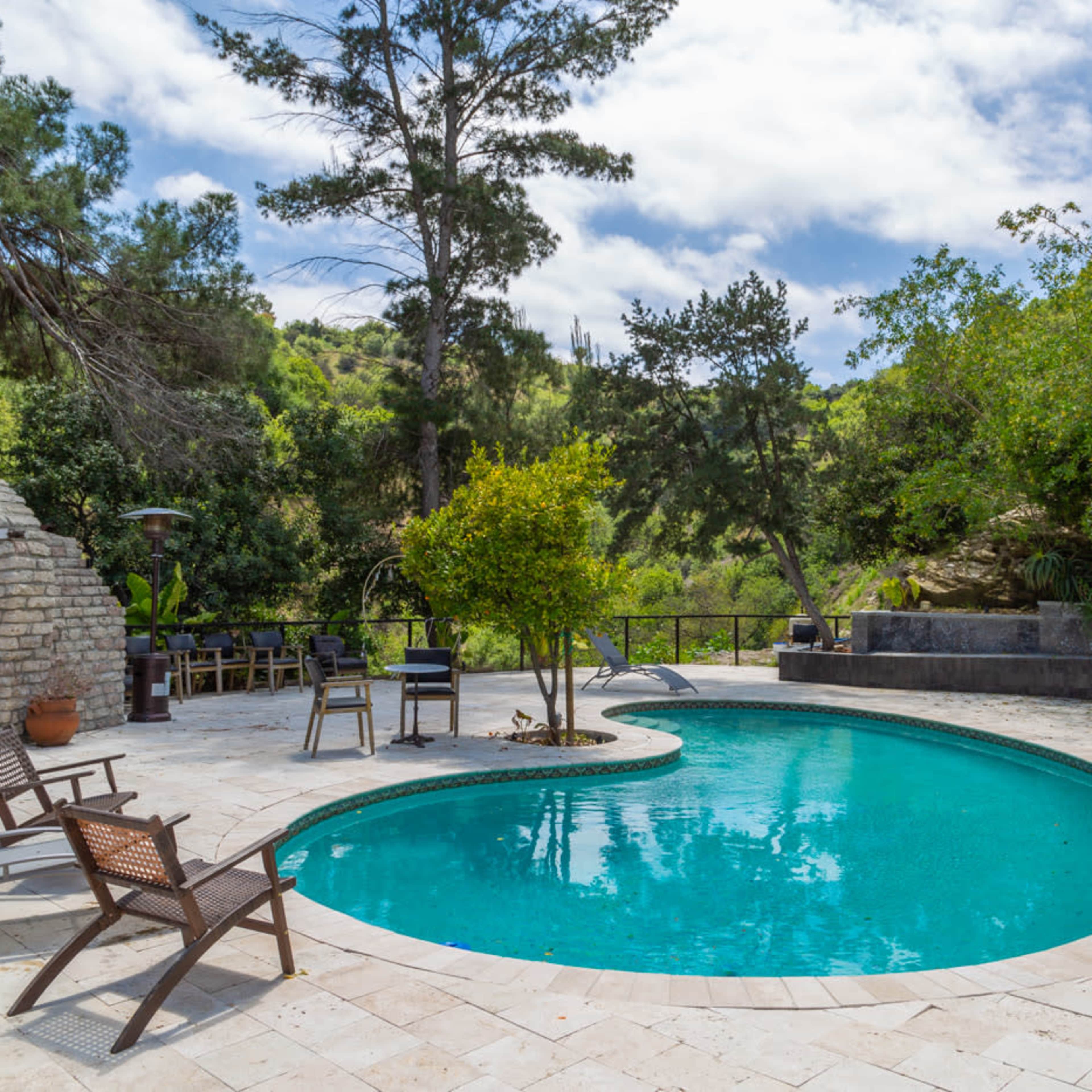 A round swimming pool surrounded by stone tiles, lounge chairs, and lush greenery in a natural setting.