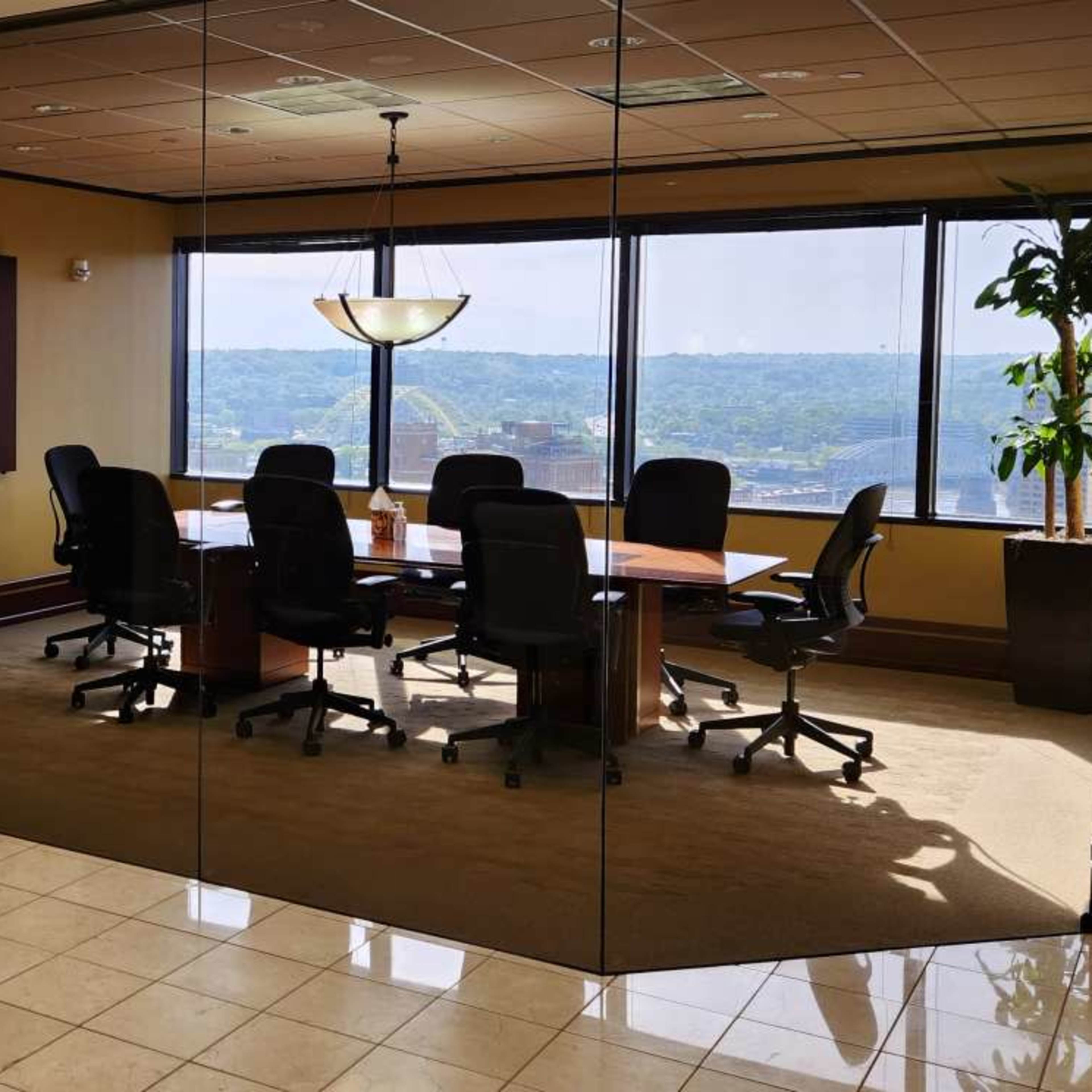 A conference room with a large table and several black office chairs is visible through glass walls, featuring large windows that overlook a distant landscape.