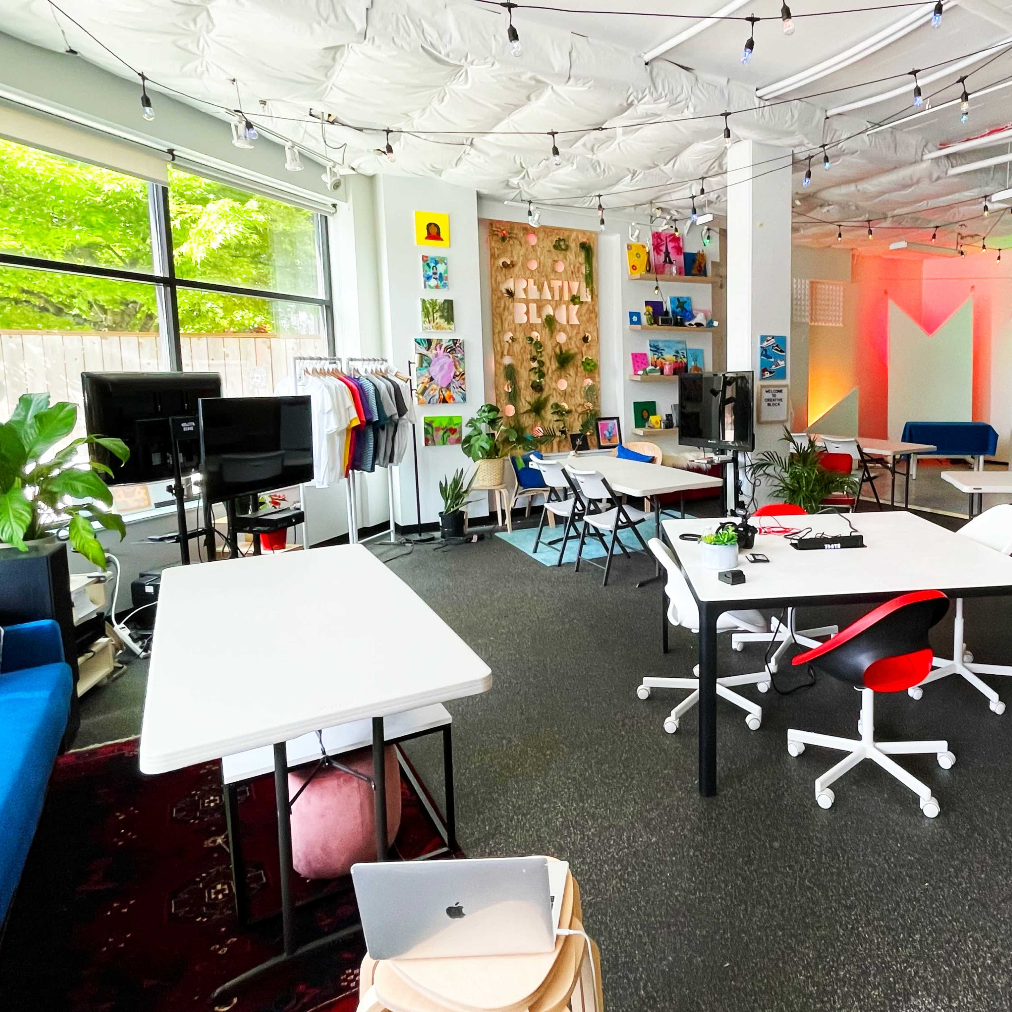 A modern workspace with multiple tables, chairs, and a colorful backdrop, featuring a mix of decorative elements and soft lighting.