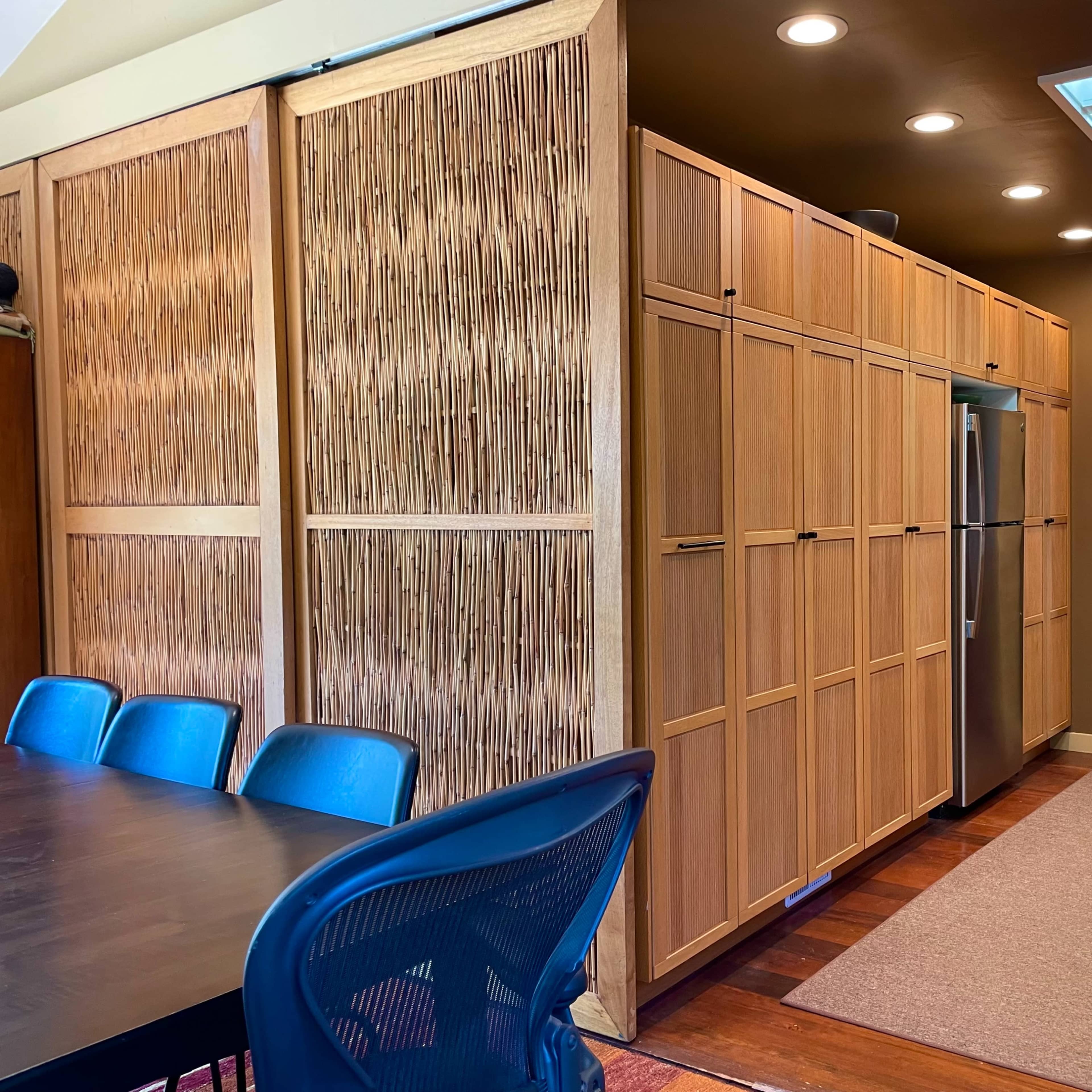 A modern kitchen with wooden cabinetry and a dining area furnished with blue chairs.