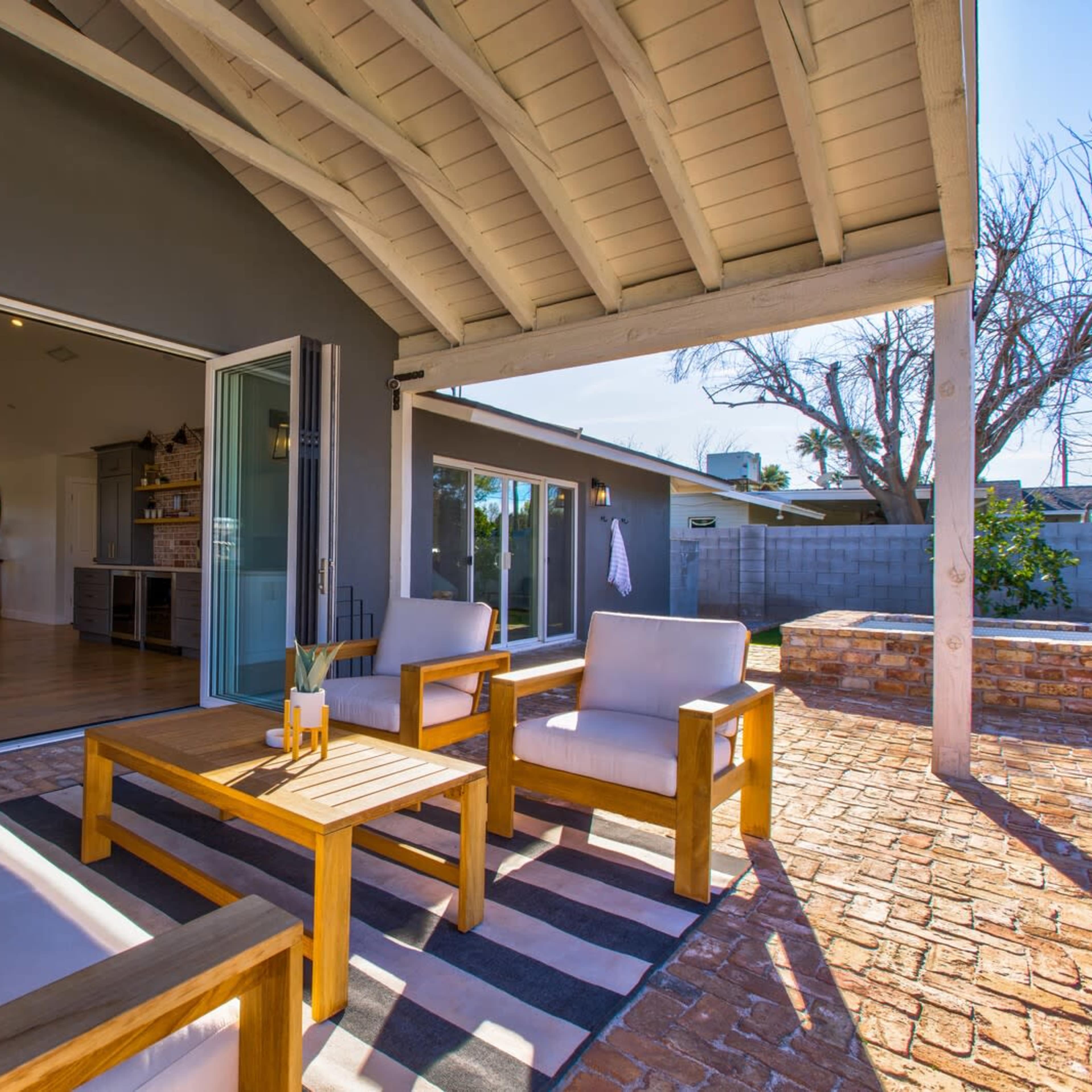 A modern outdoor seating area with wooden furniture and an open view of a sunlit interior space.