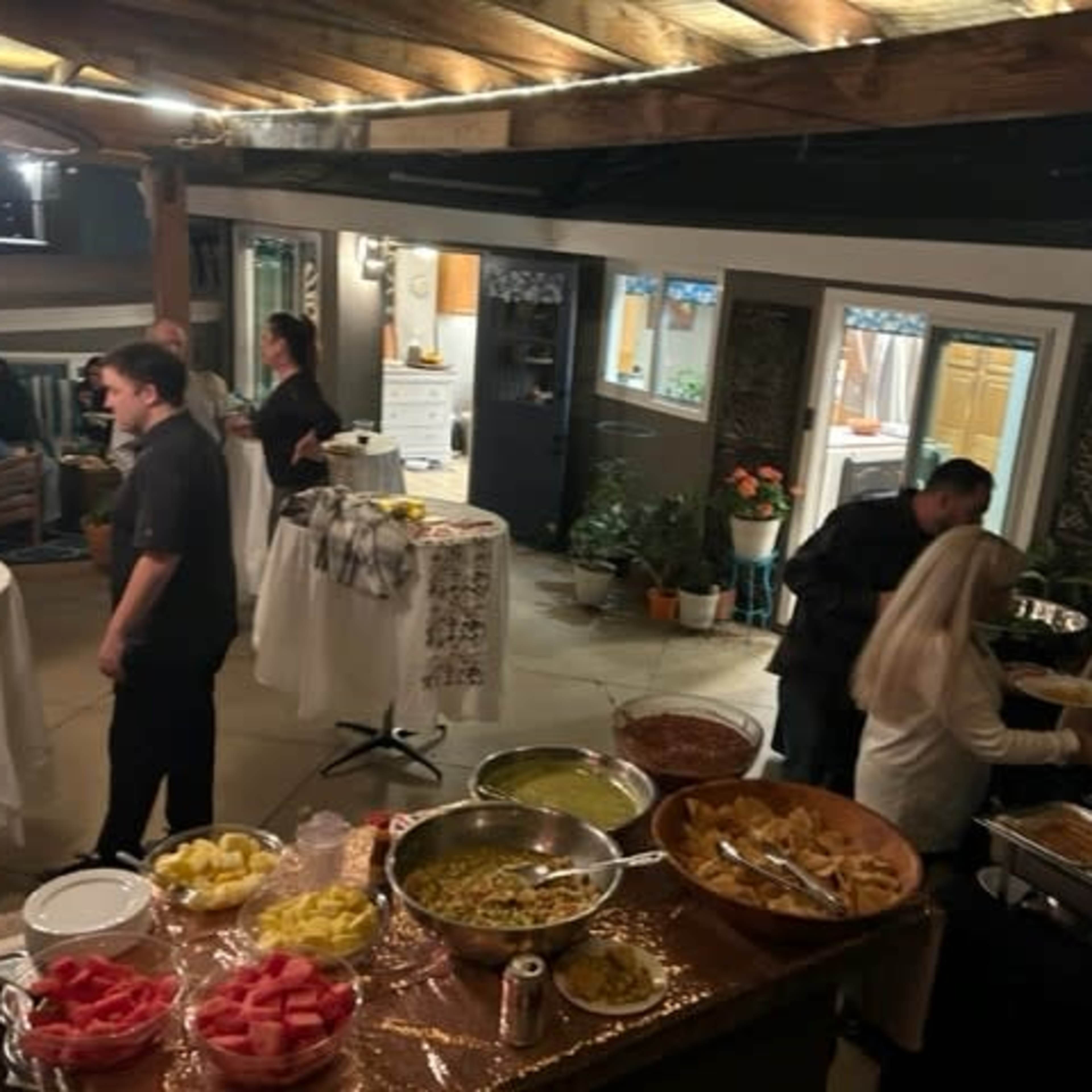 A gathering is taking place in an indoor-outdoor space with guests enjoying a buffet of food and drinks.