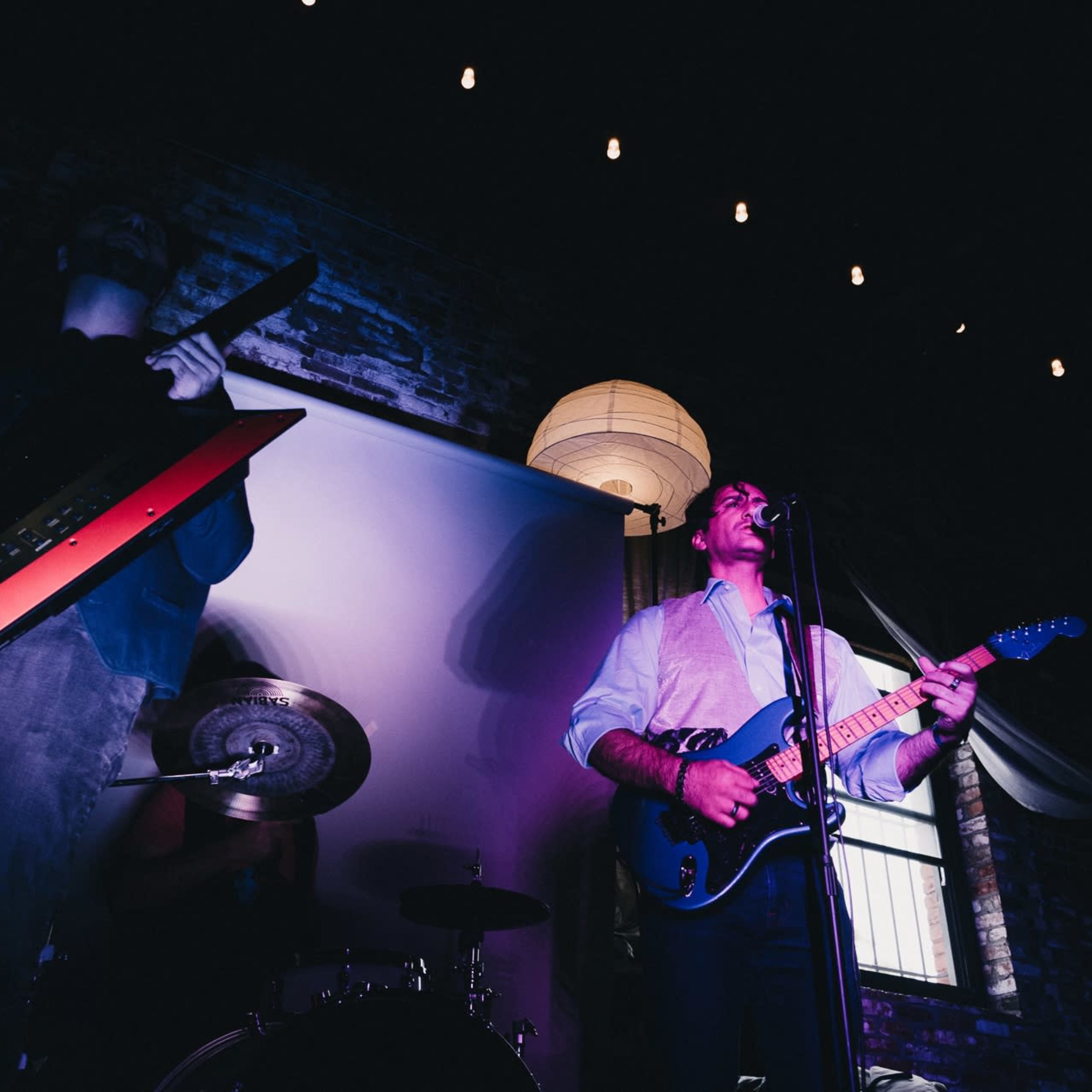 A band performs on a dimly lit stage with a keyboard player and a guitarist.