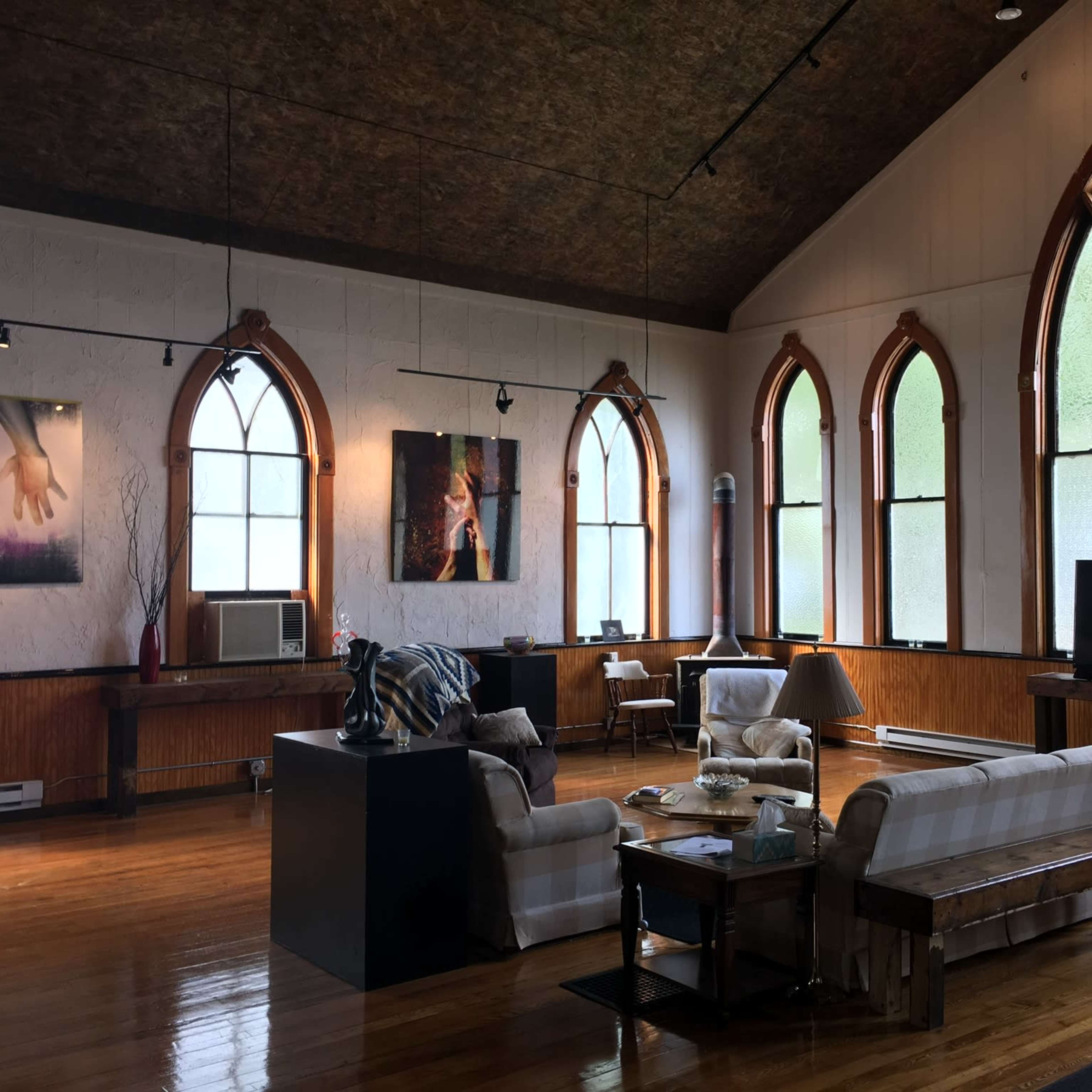 A spacious room with high ceilings, large arched windows, wooden flooring, and a seating area featuring a couch and coffee table.