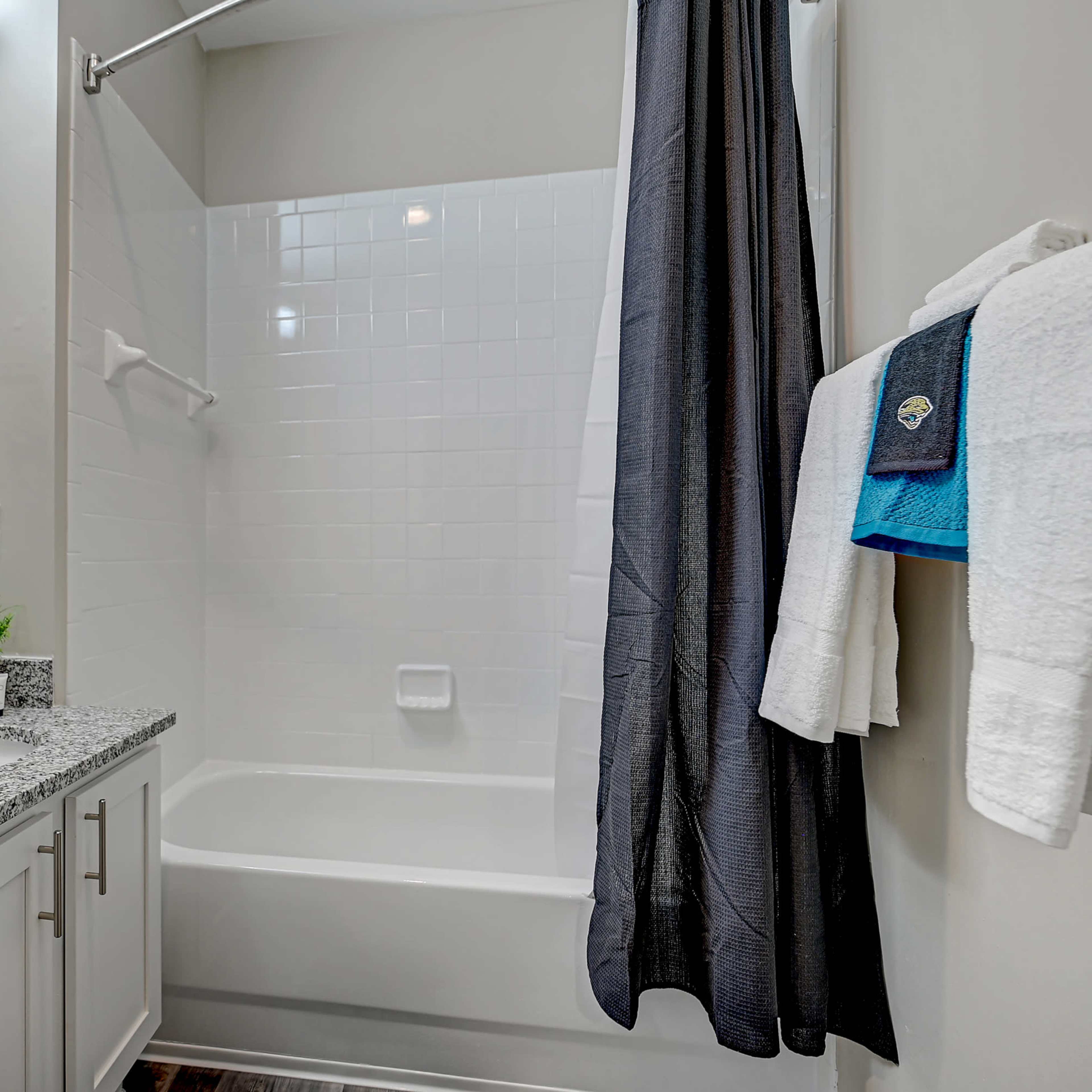 A clean bathroom features a bathtub with a shower curtain, a granite countertop with a sink, and neatly arranged towels.