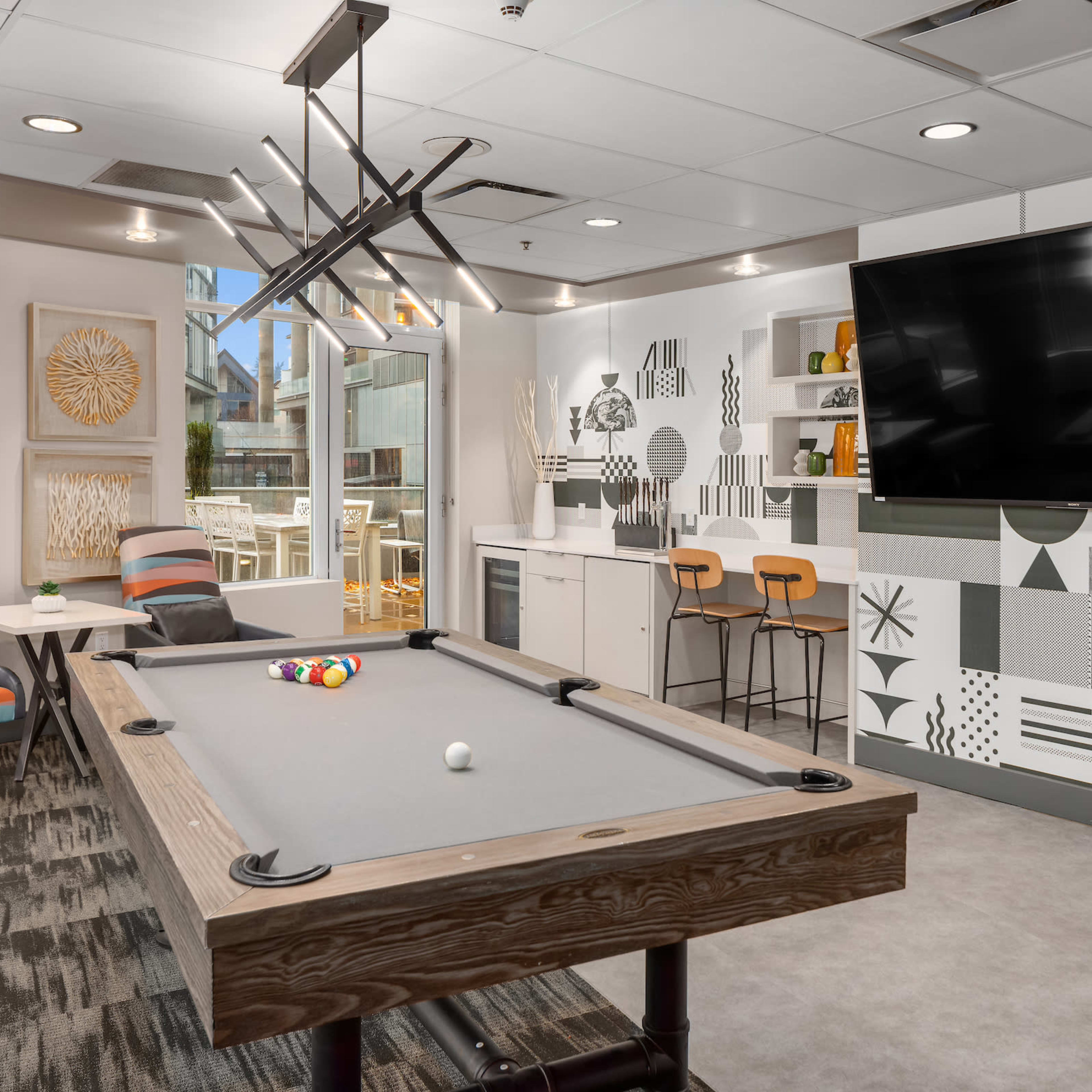 A modern game room featuring a pool table, seating area, and a large wall-mounted television with a patterned mural.