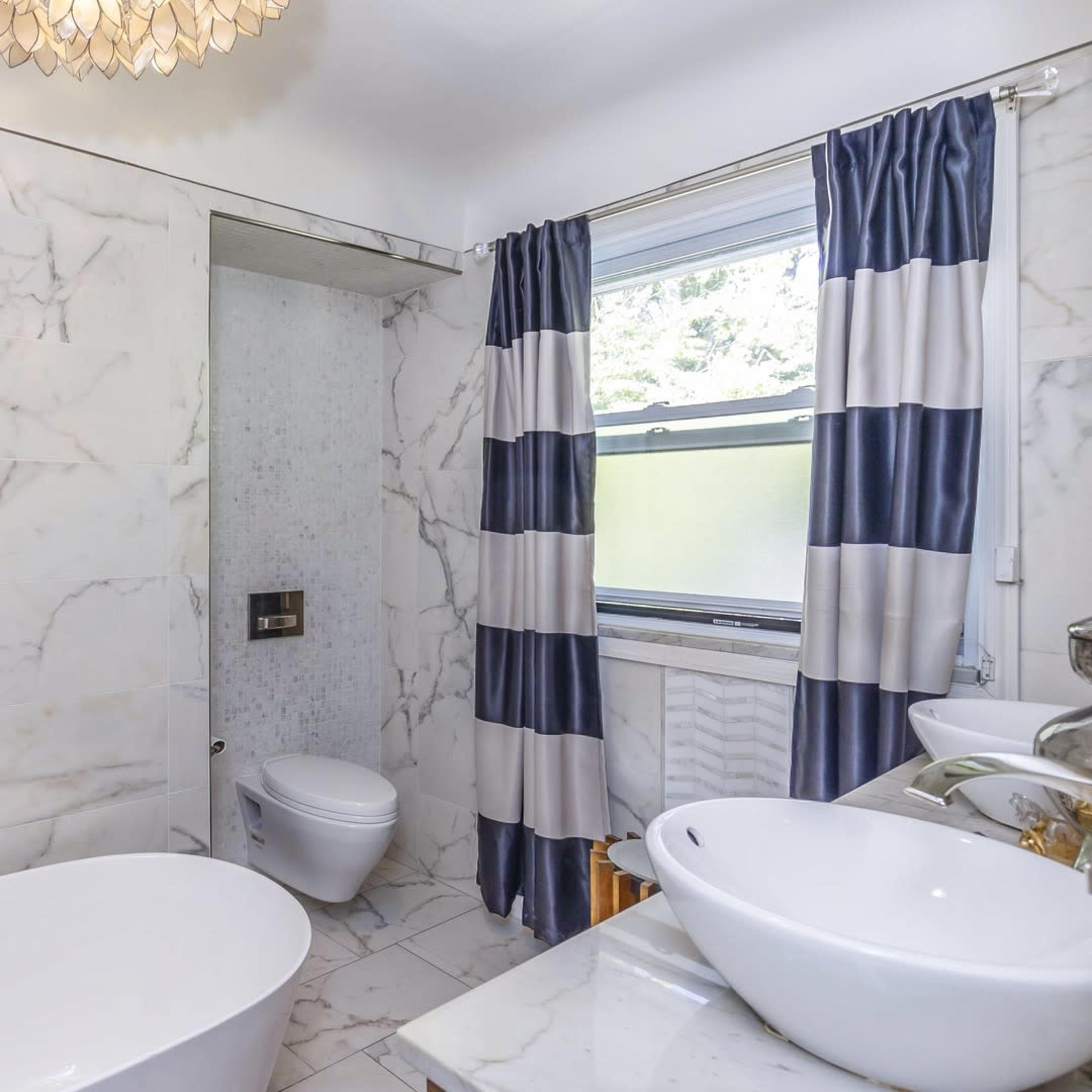 A modern bathroom featuring a freestanding bathtub, a glass shower enclosure, and marble walls with dark blue and white striped curtains.