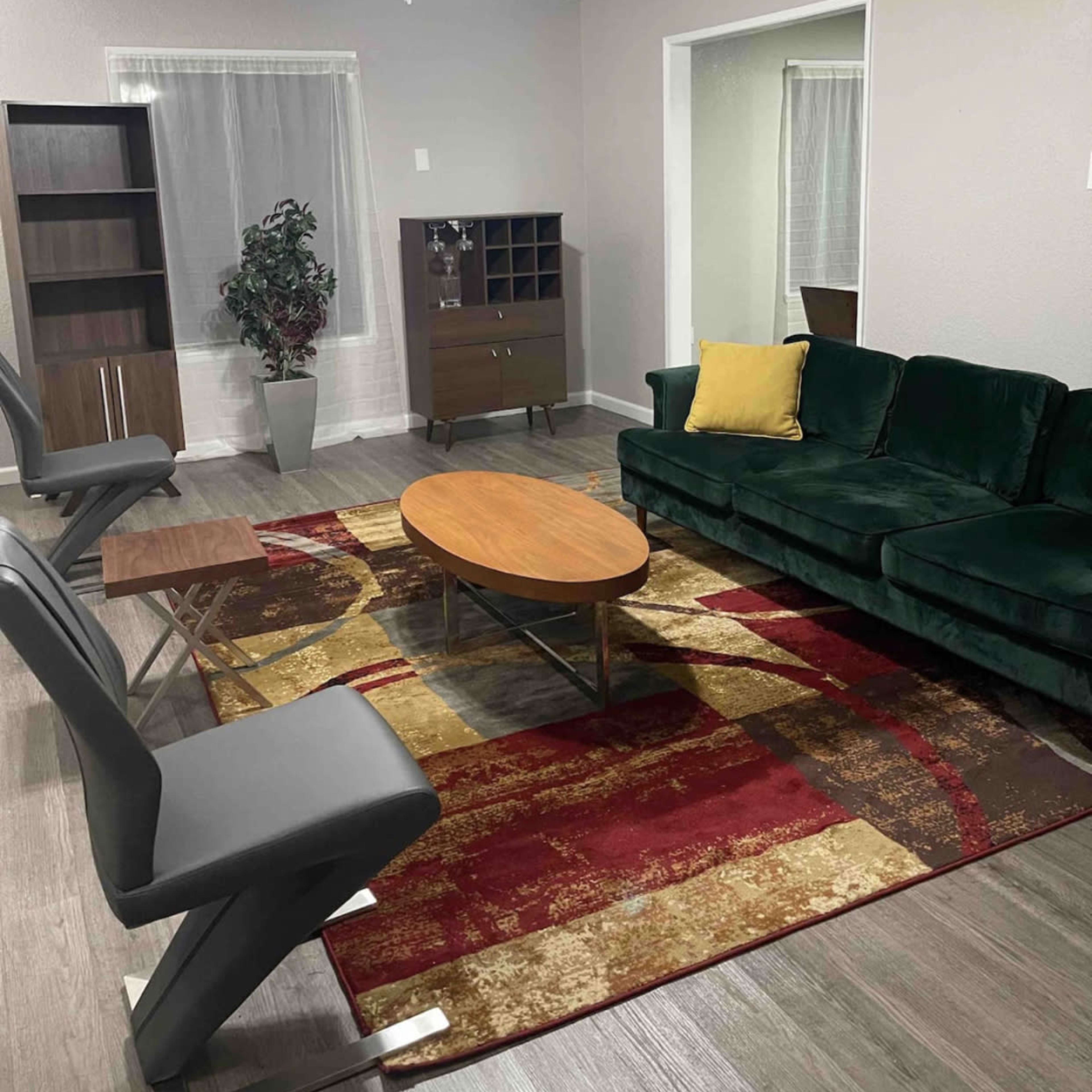 A living room with a green sofa, a round coffee table, two gray chairs, and a patterned rug on the floor.