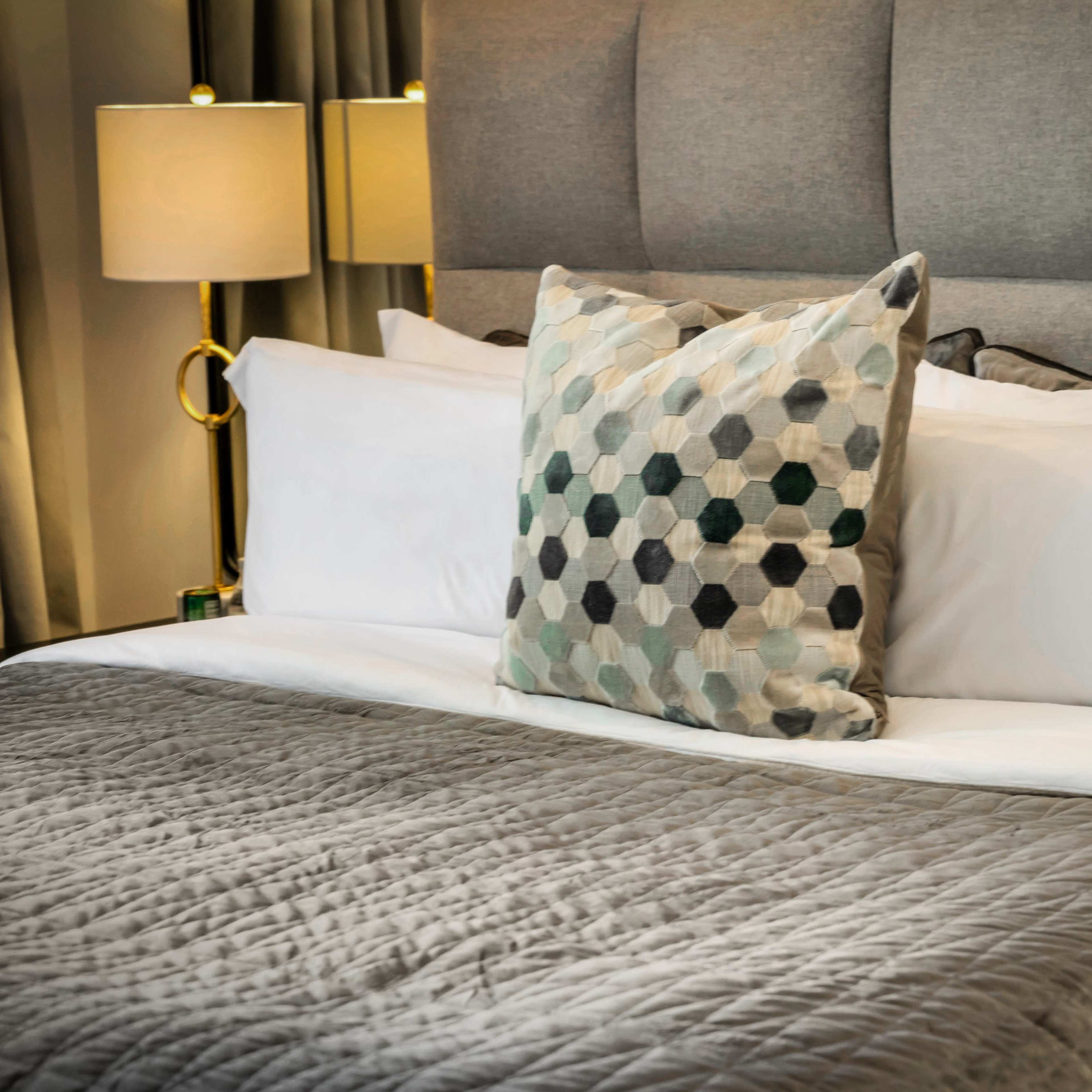 A neatly made bed features a gray quilt and a decorative pillow with a geometric pattern.