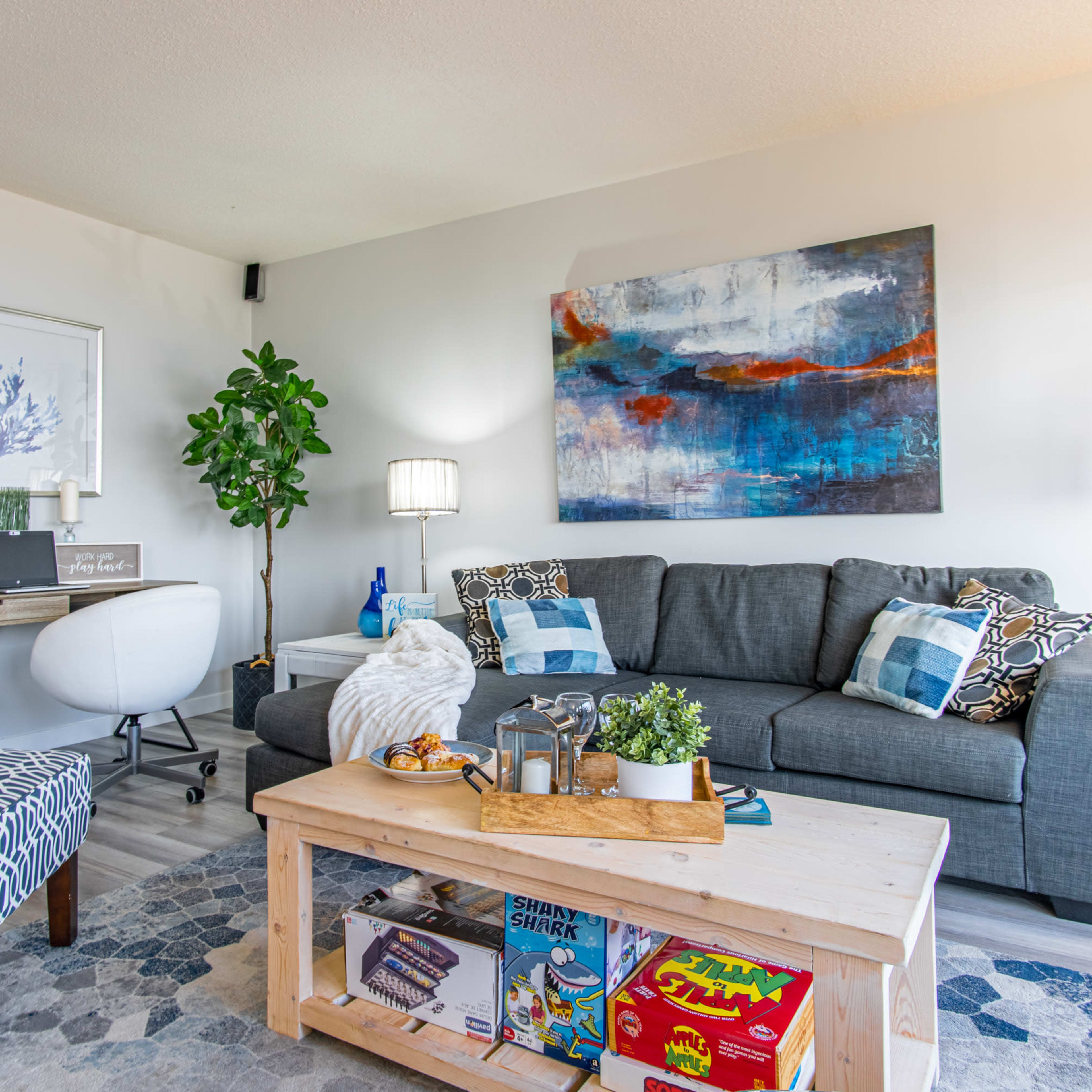 A modern living room with a gray sofa, a wooden coffee table displaying magazines, and a patterned armchair beside a small desk.