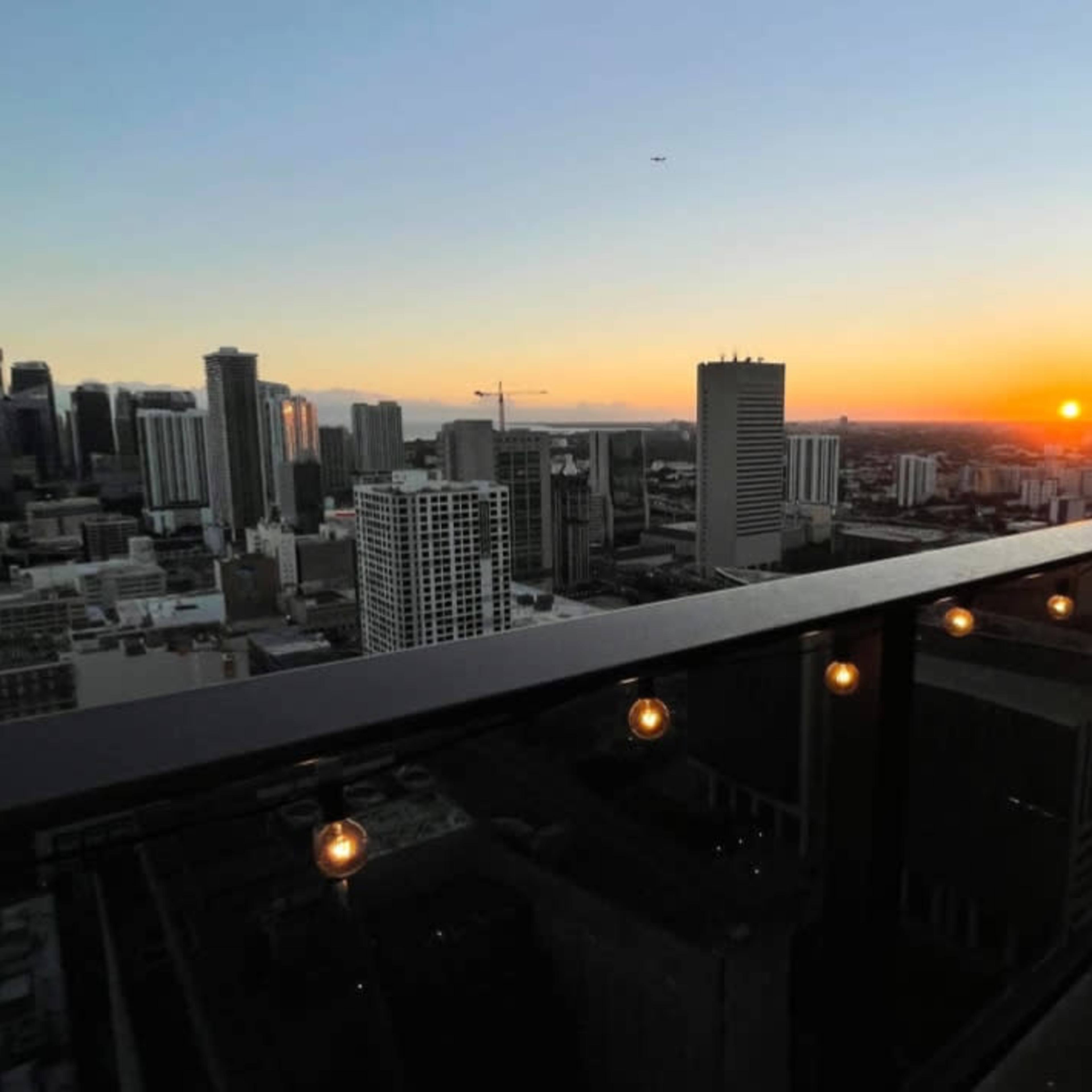 A city skyline at sunset, with a balcony adorned with string lights in the foreground.
