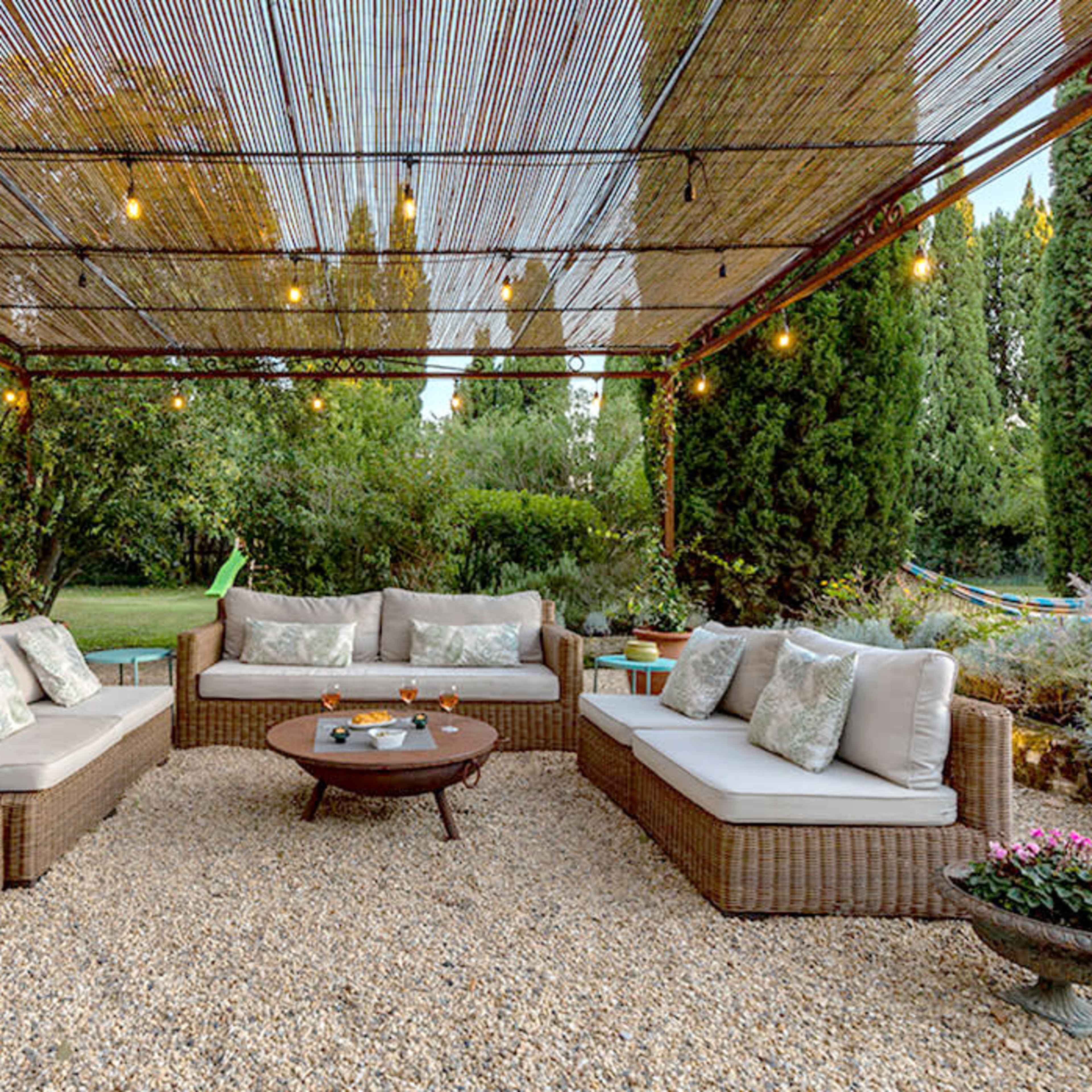 A patio area features a seating arrangement of wicker furniture with gray cushions around a circular table, under a bamboo canopy adorned with string lights.