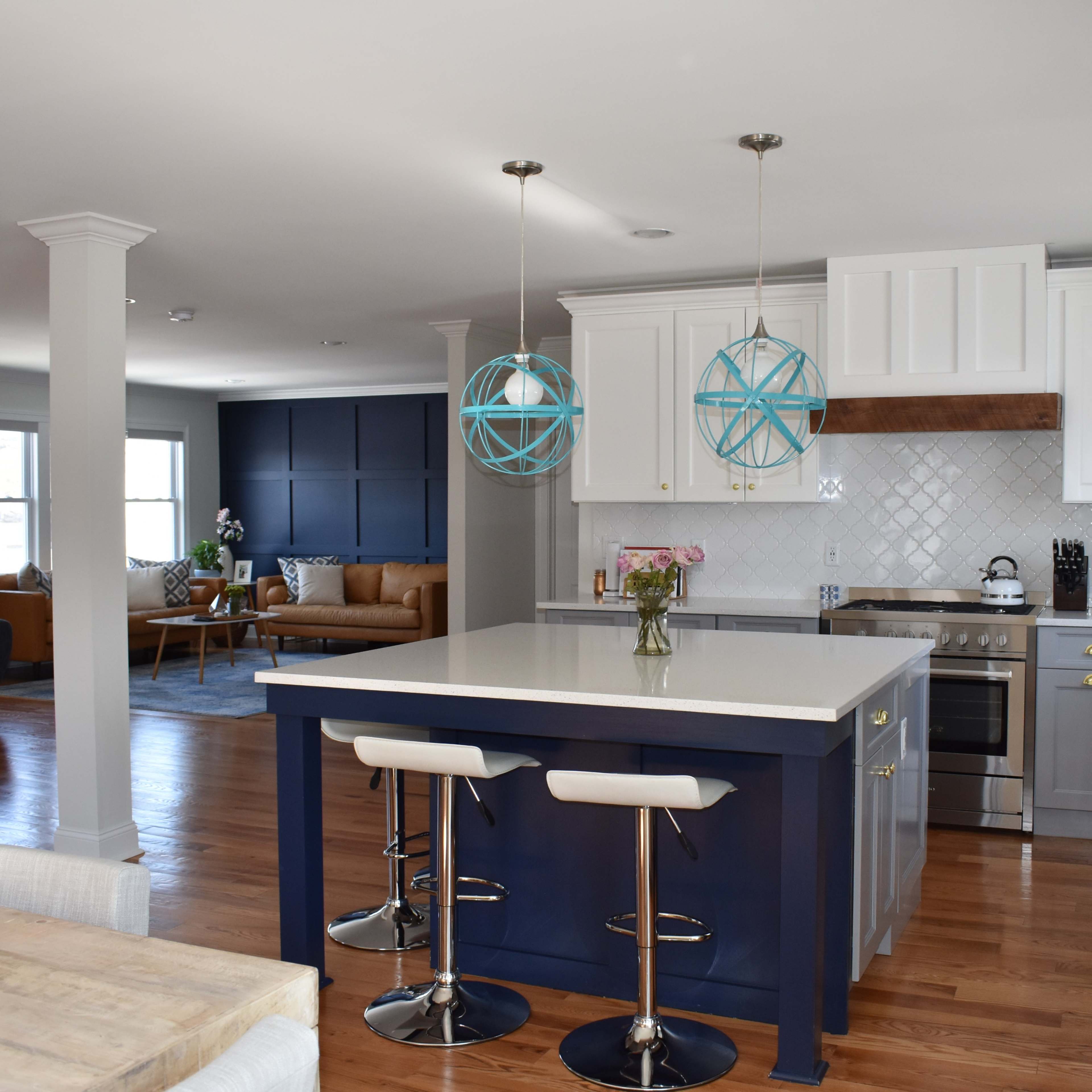 A modern kitchen with a large island, blue pendant lights, and an open layout connecting to a living area furnished with a sofa and chairs.