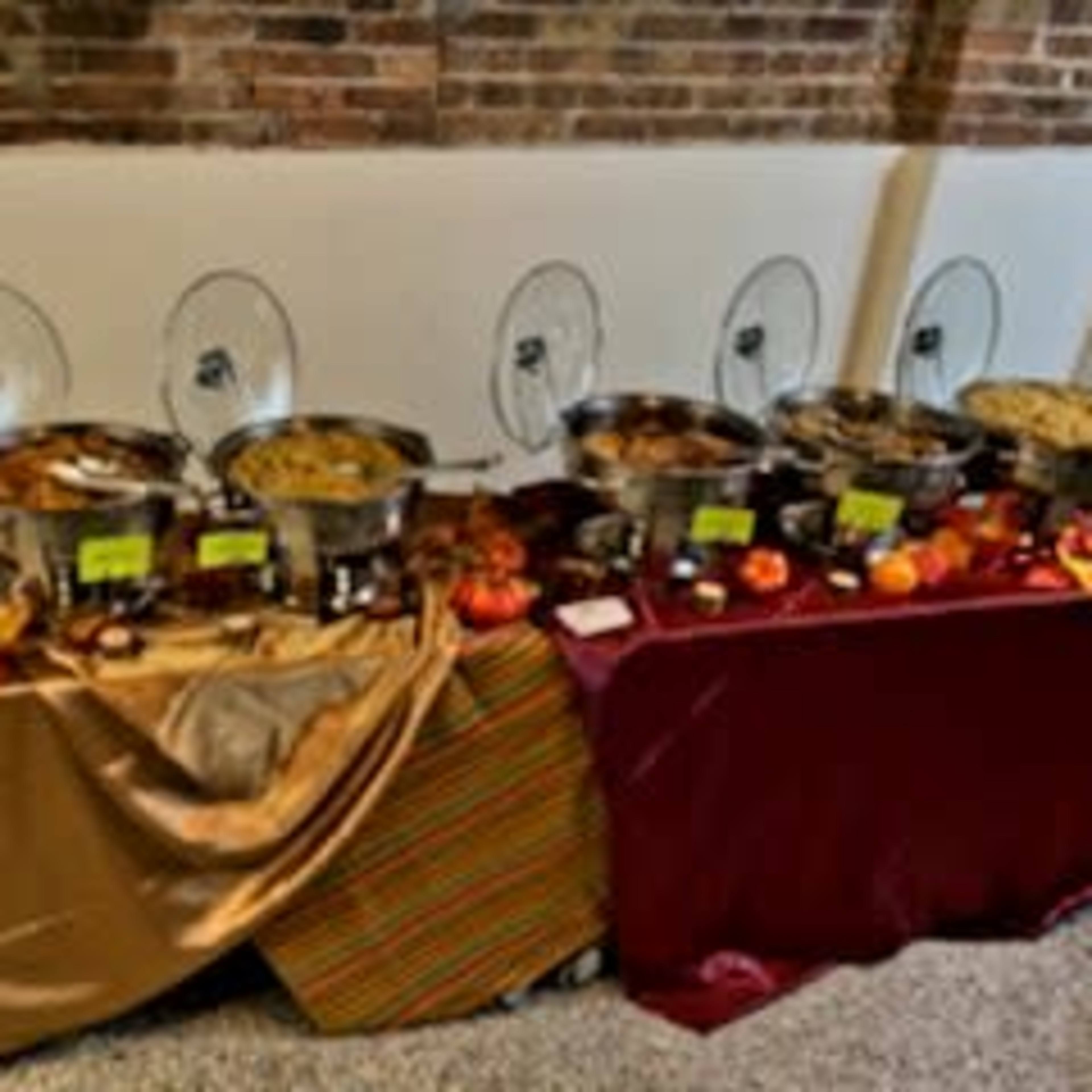A long serving table displays various buffet trays filled with food, set against a brick wall.