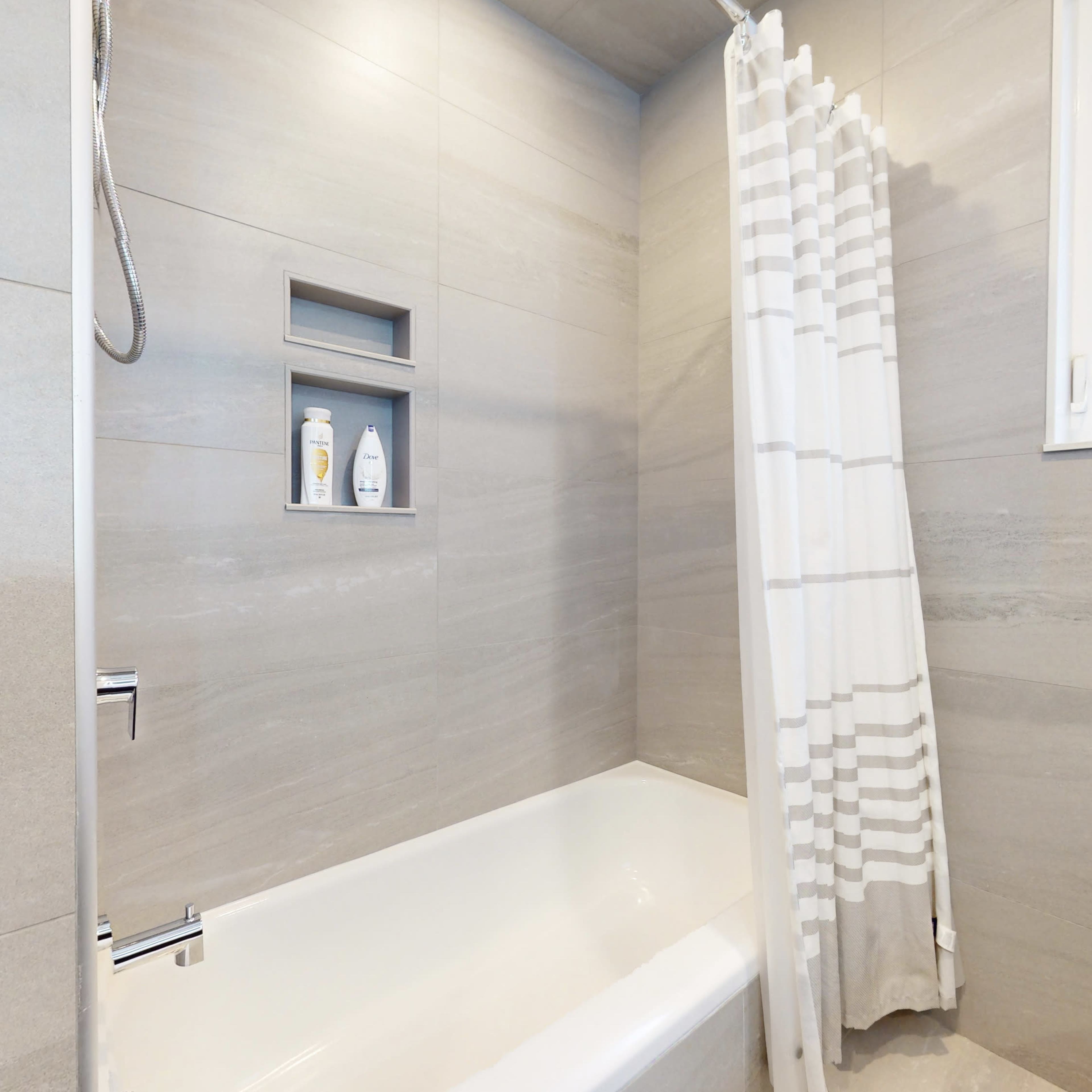 A modern bathroom featuring a bathtub with a shower, gray tiled walls, and a striped shower curtain.