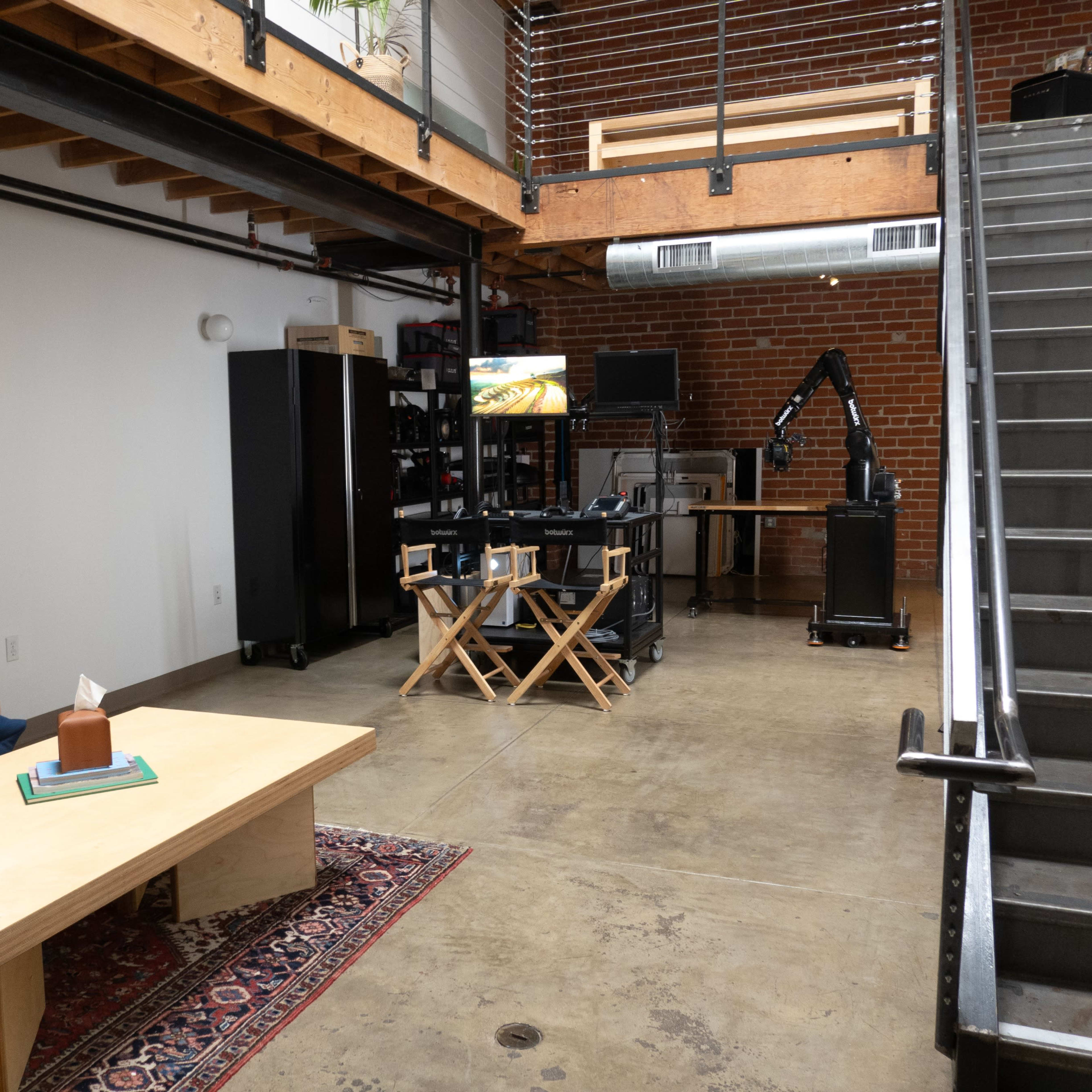 A spacious loft-like interior with a blue couch, a wooden coffee table, and a staircase leading to an upper level.