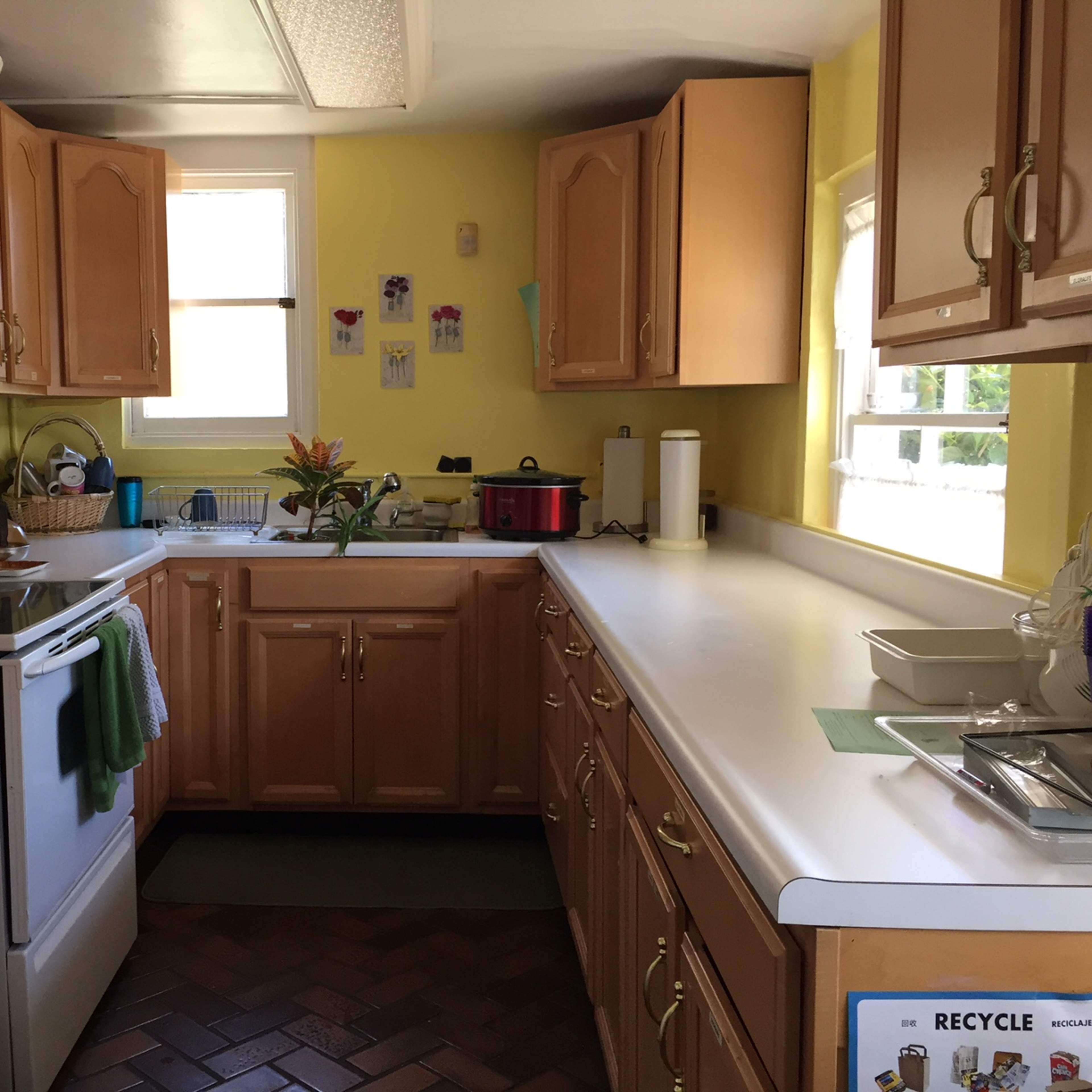 A bright kitchen features wooden cabinets, a refrigerator, a stove, and a work area with flowers on the counter.