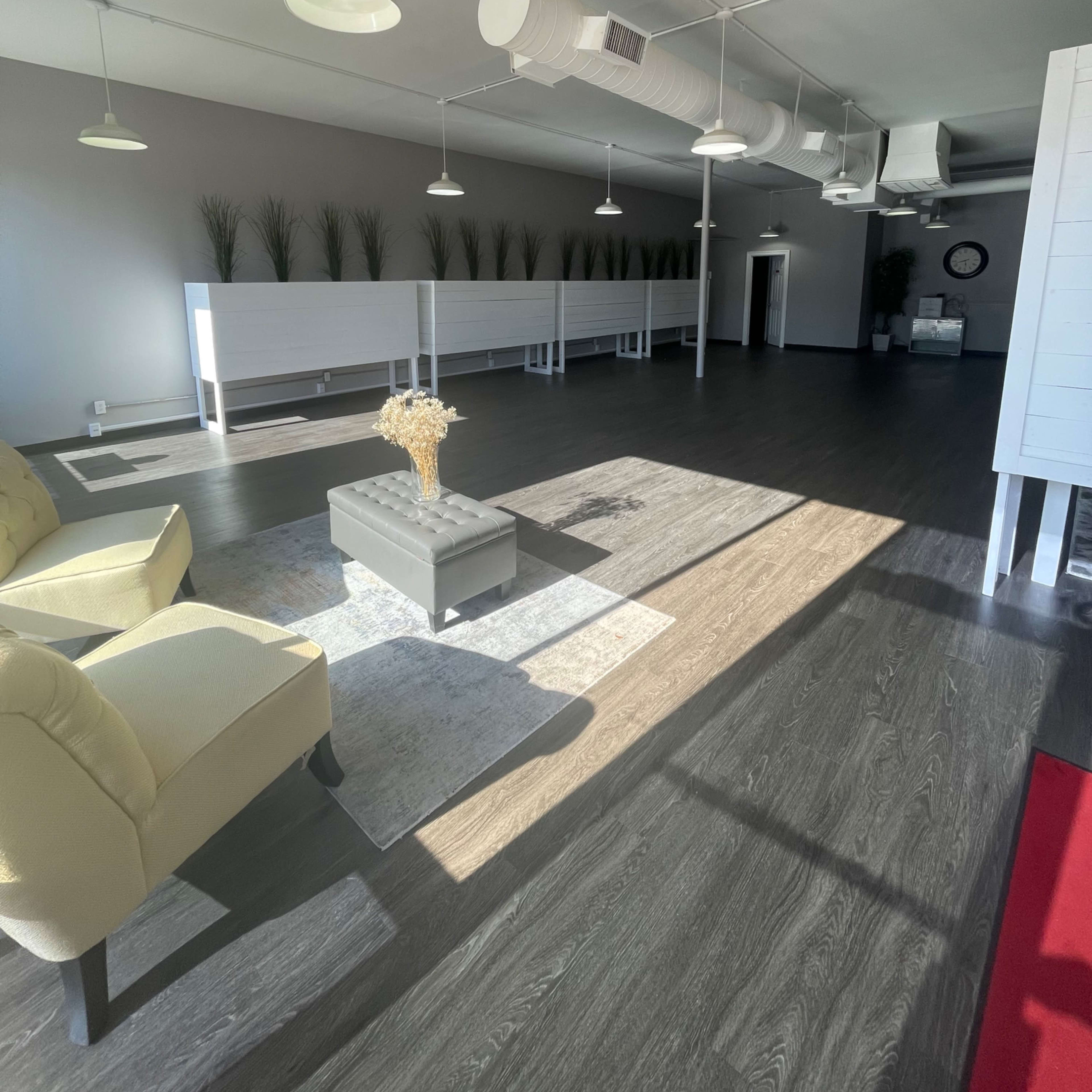 A spacious, brightly lit interior with hardwood flooring, white display tables, and a seating area featuring a yellow chair and decorative elements.