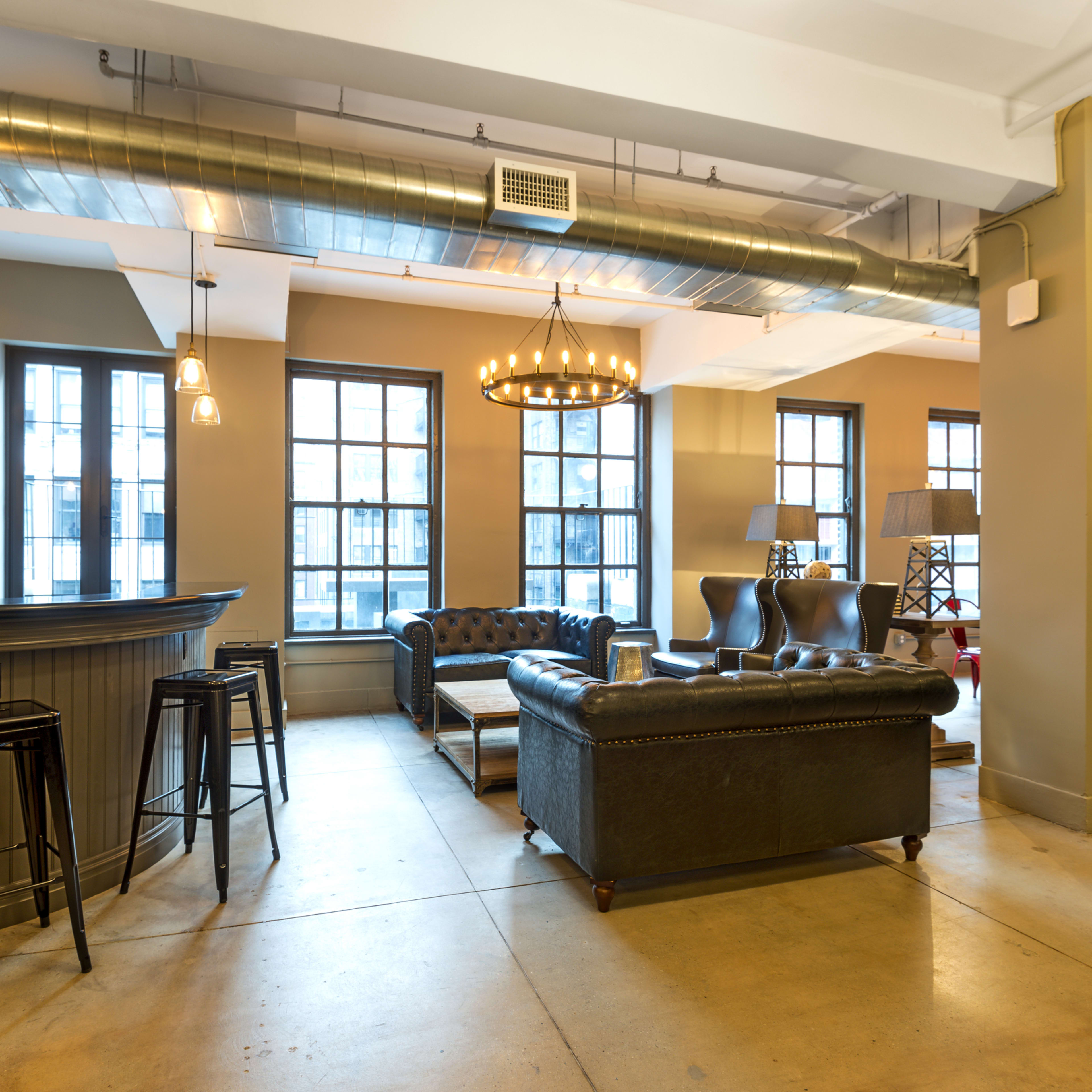 A modern lounge area with a bar, leather sofas, and tall windows that allow natural light to fill the space.