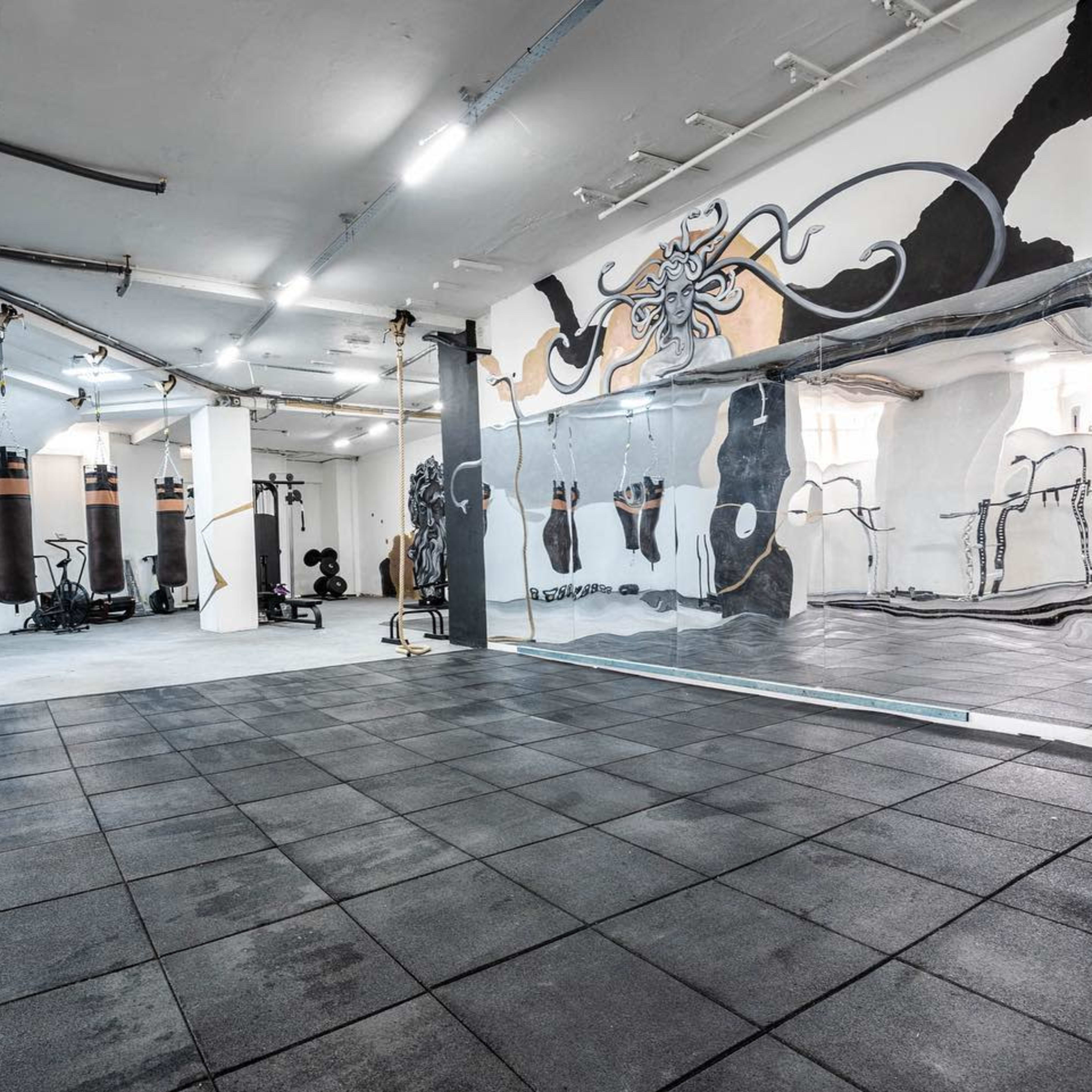 A spacious gym interior featuring rubber flooring, wall mirrors, and exercise equipment along with a mural of an octopus.