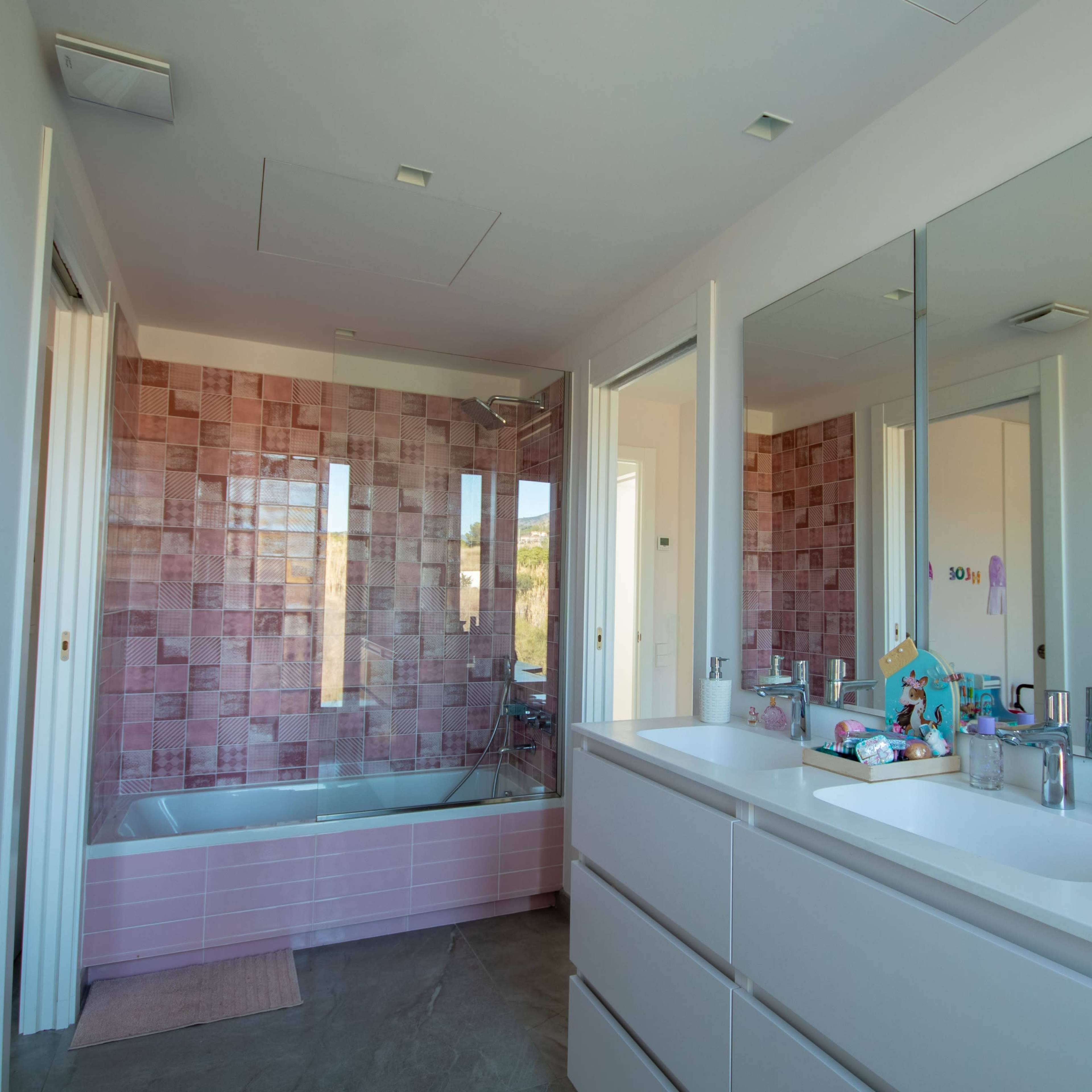 A modern bathroom with a pink tiled wall, a bathtub, and dual sinks with large mirrors above them.
