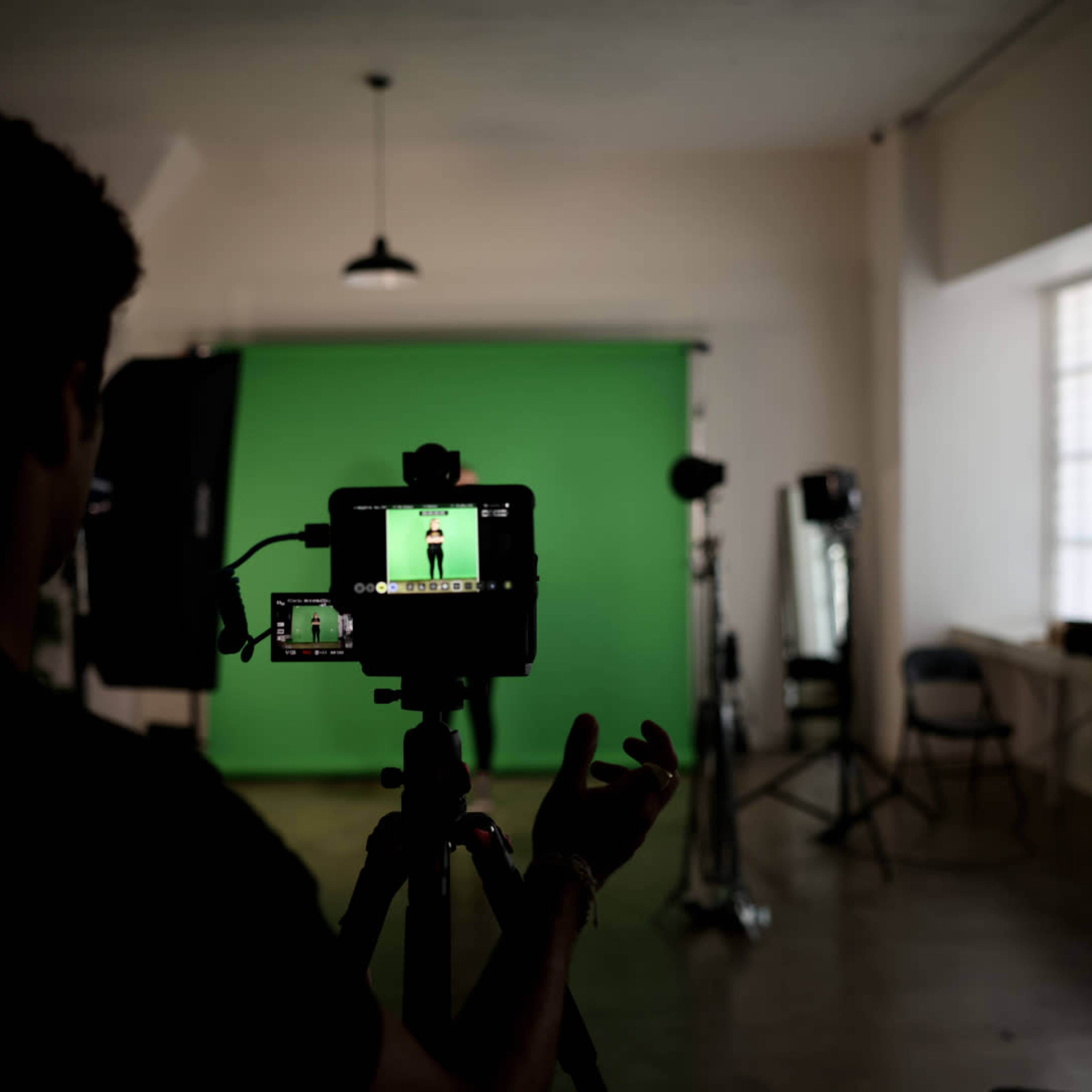 A person operates a camera in front of a green screen in a studio setting.