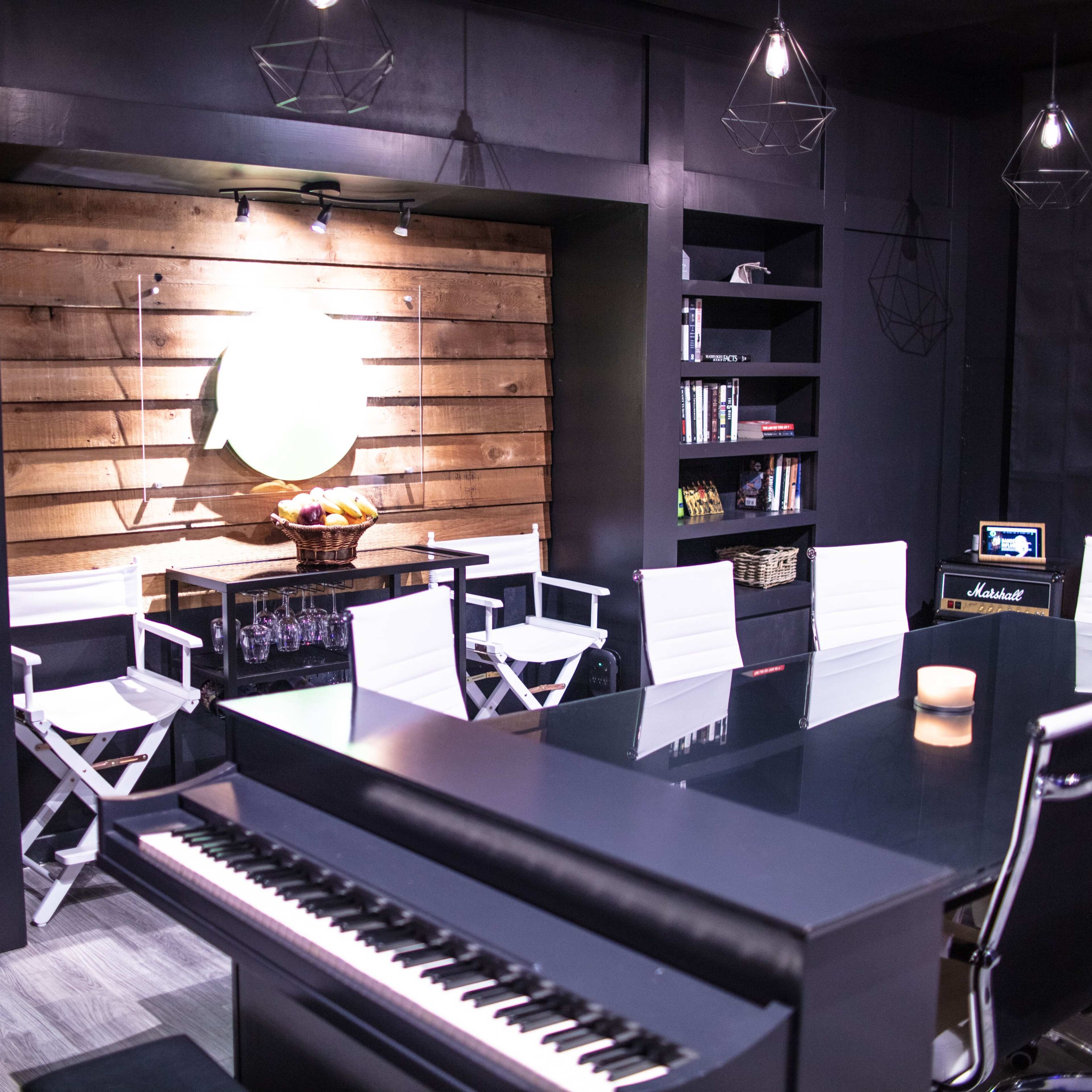 A modern room featuring a piano, a row of white chairs, wooden bookshelves filled with books, and several clocks on the wall.