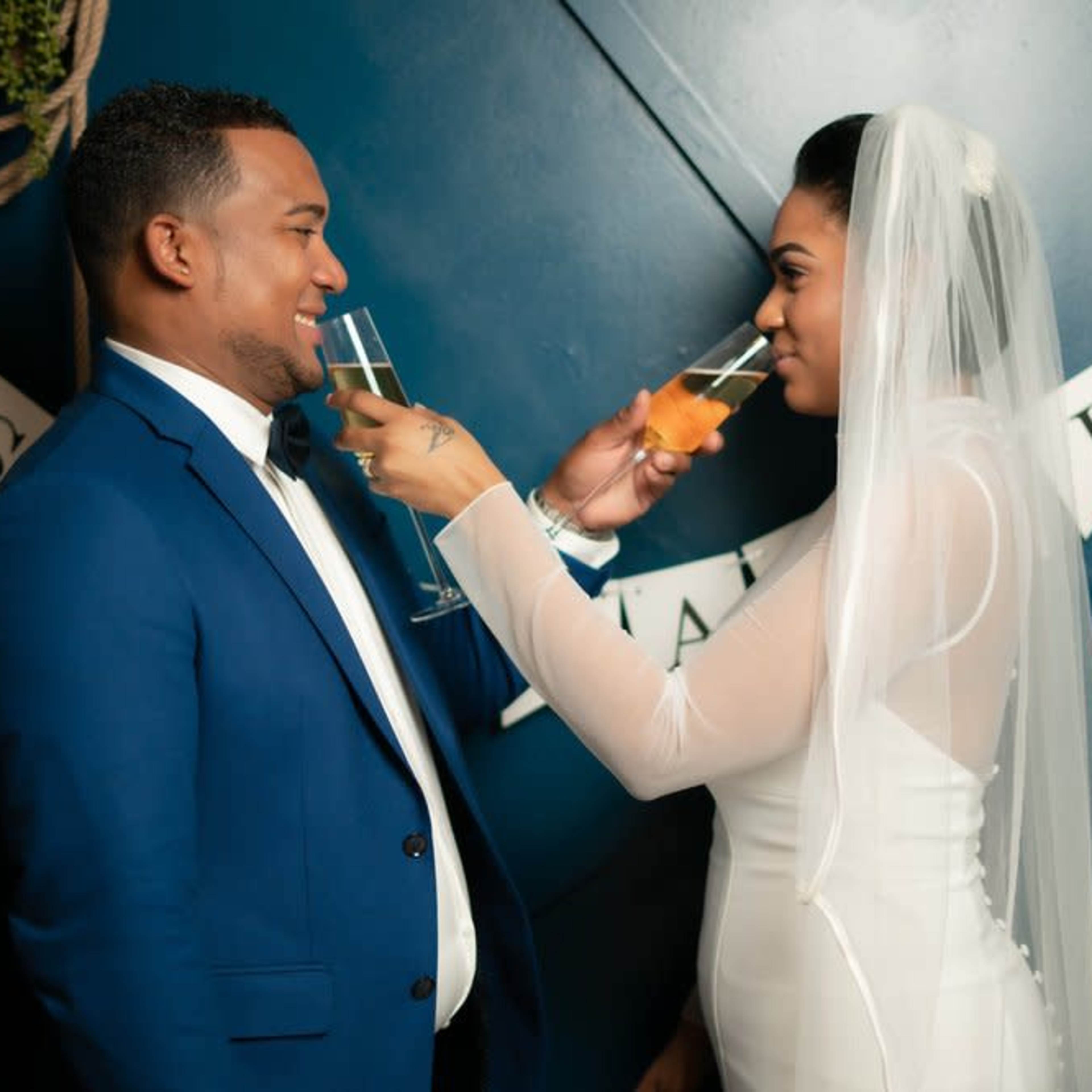A couple in formal attire toasts with glasses in front of a "Just Married" banner.