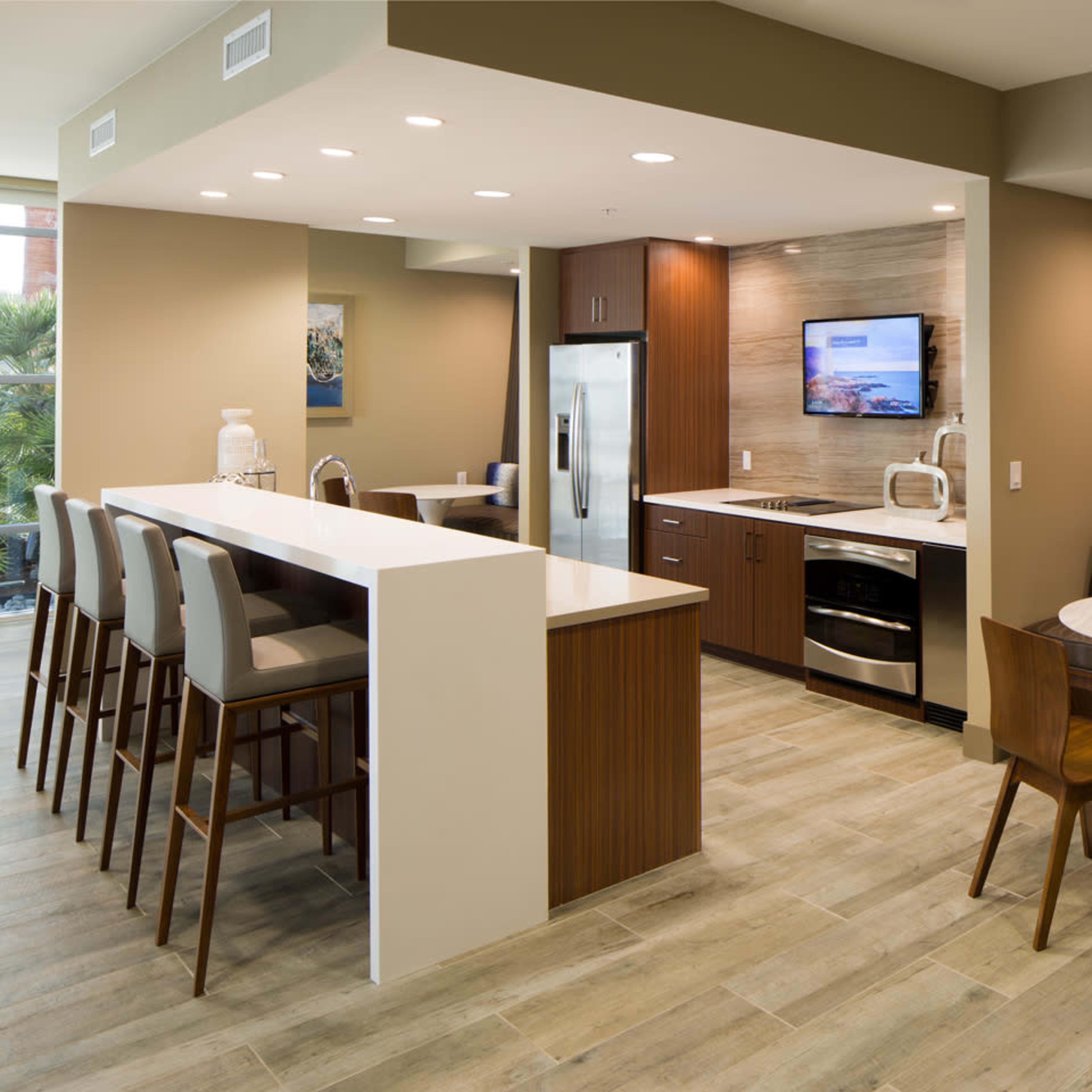 A modern kitchen area features a central island with bar stools, stainless steel appliances, and a dining table in a well-lit, open layout.