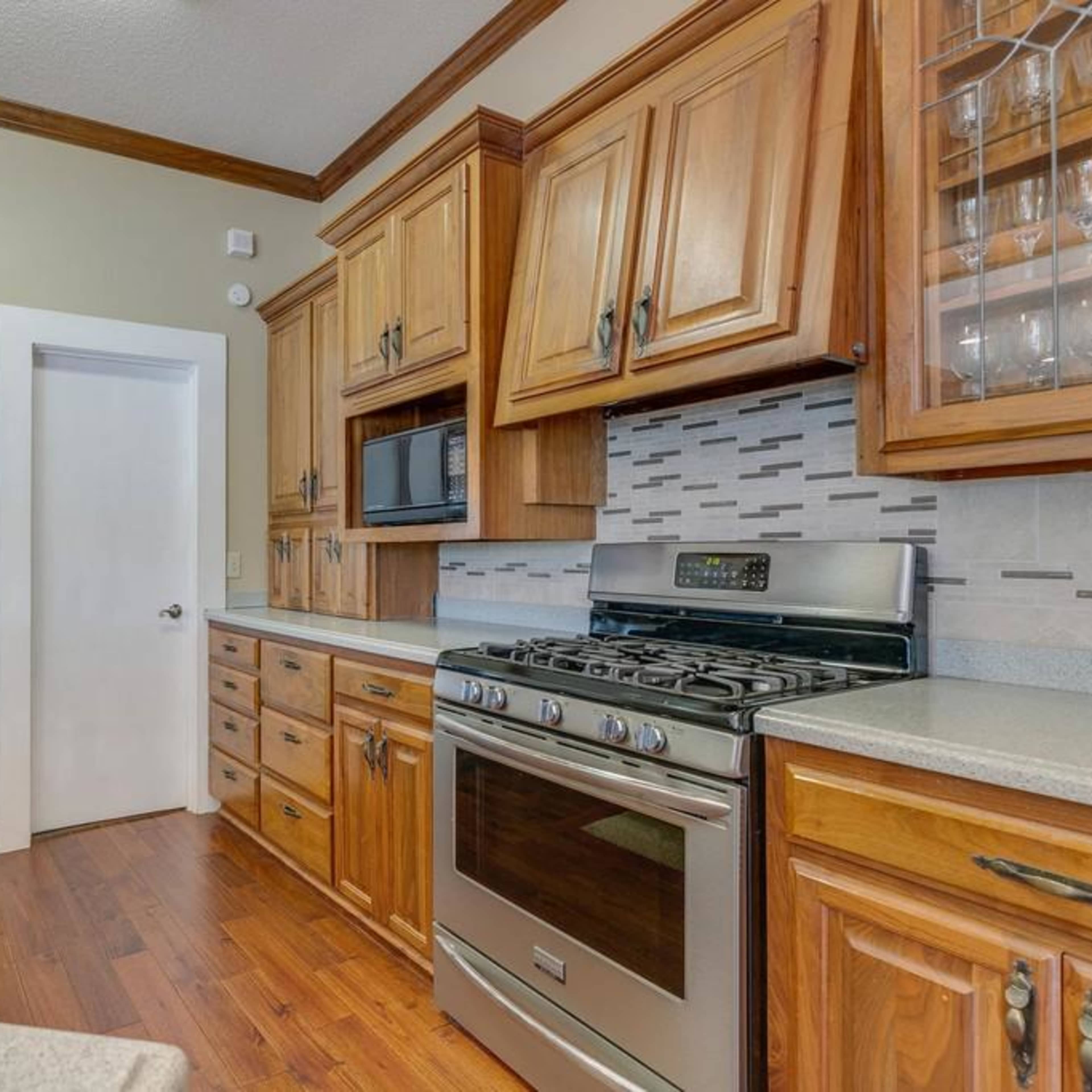 A kitchen with wooden cabinets, stainless steel appliances, and a gas stove, featuring a light-colored countertop and a door leading to another room.