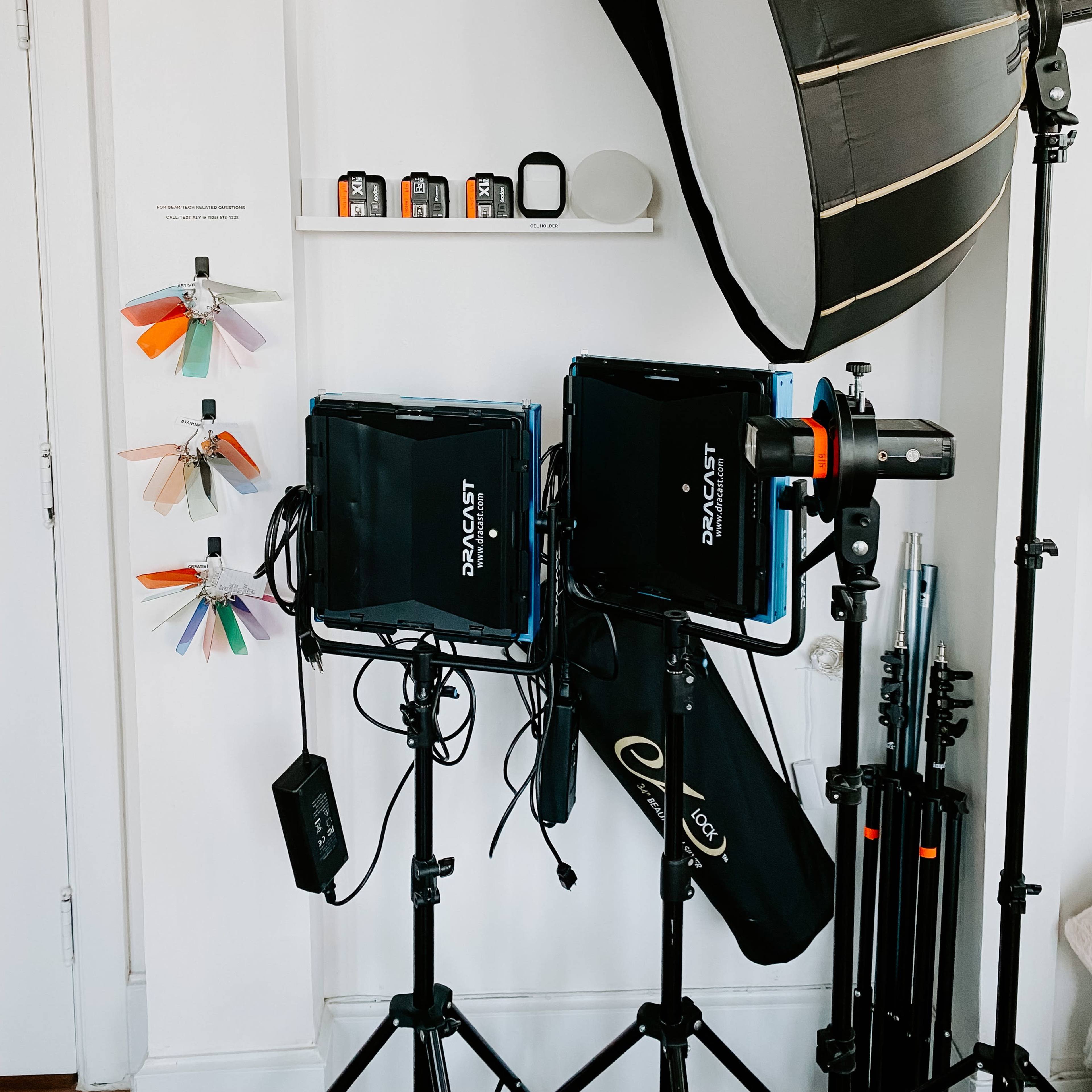 A photography setup with two softbox lights on stands, a light meter, and a shelf displaying color samples and equipment.
