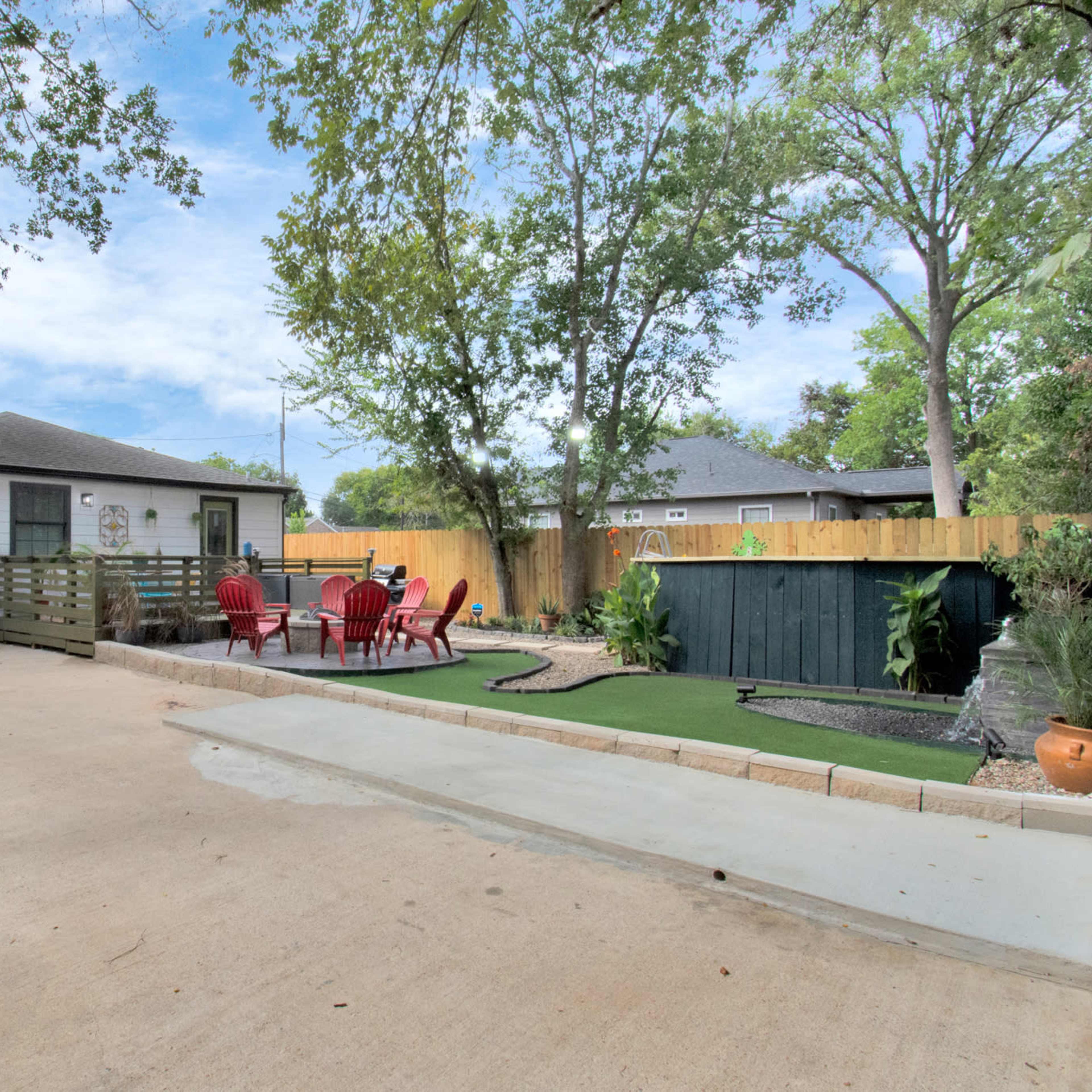 A single-story house with a fenced patio area containing red chairs and landscaping features is situated beside a wide driveway.