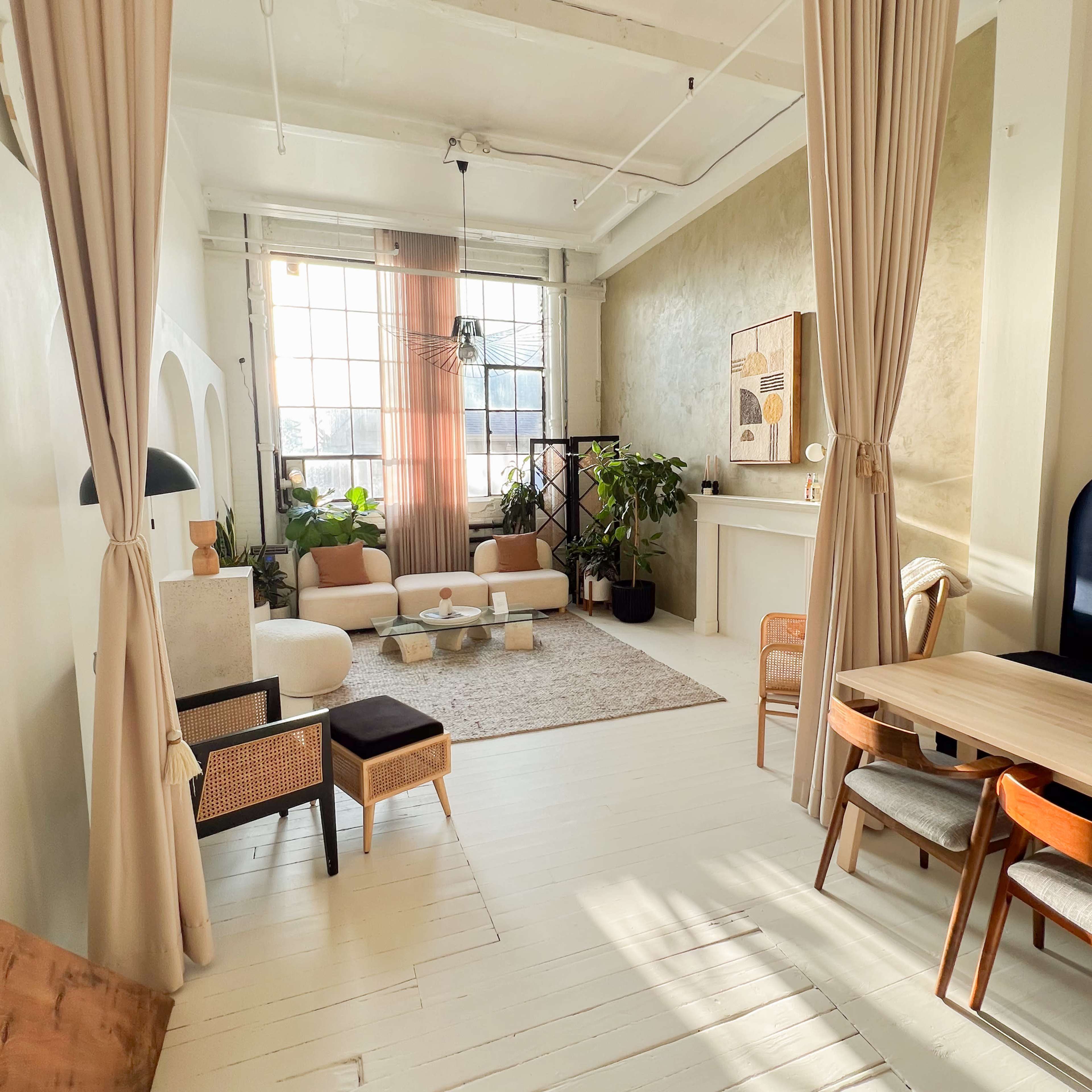 A bright, modern living space with light-colored walls, a large window, and a mix of seating options, including a round coffee table and a dining area.