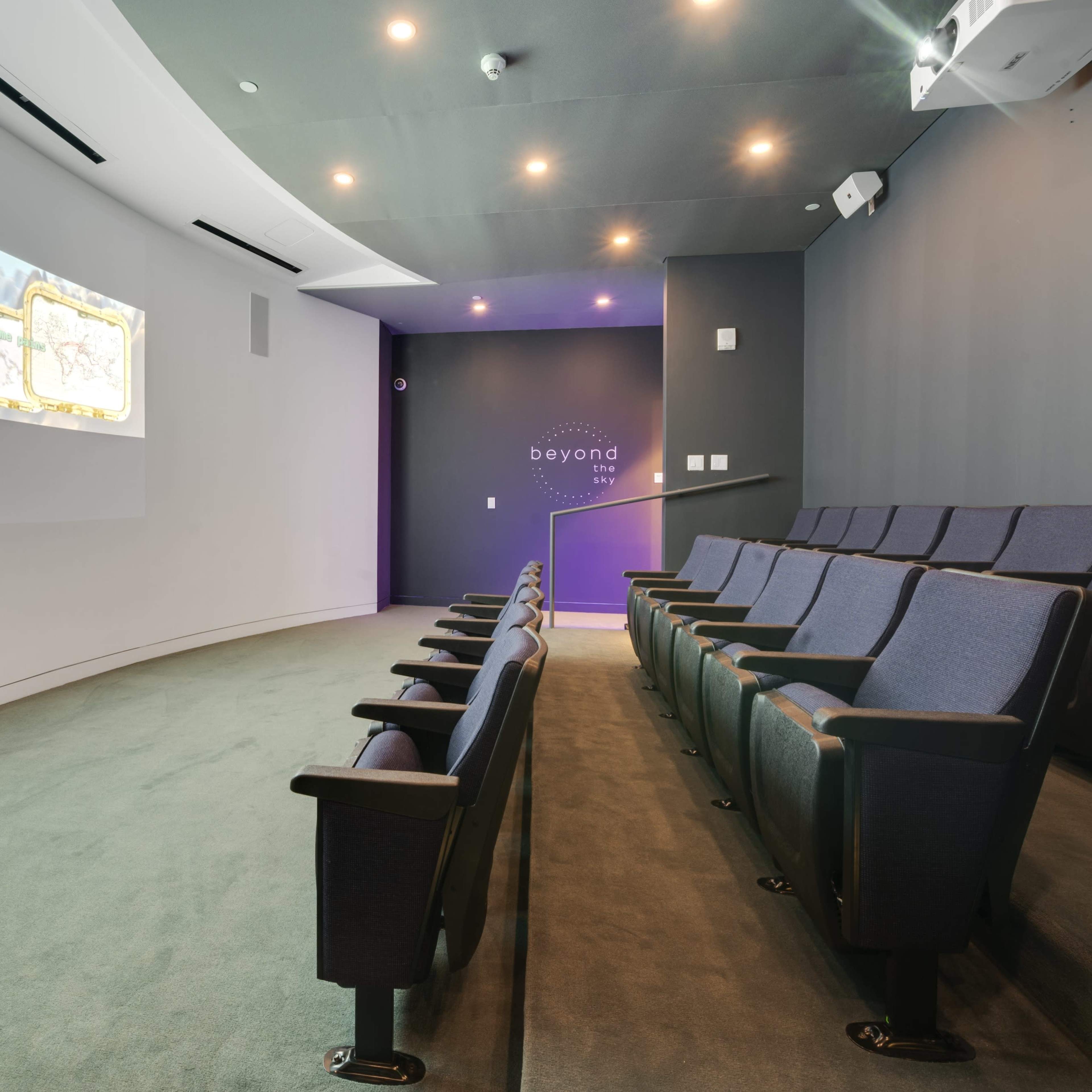 A small, modern theater with tiered seating and a large screen displaying animated visuals on one wall.