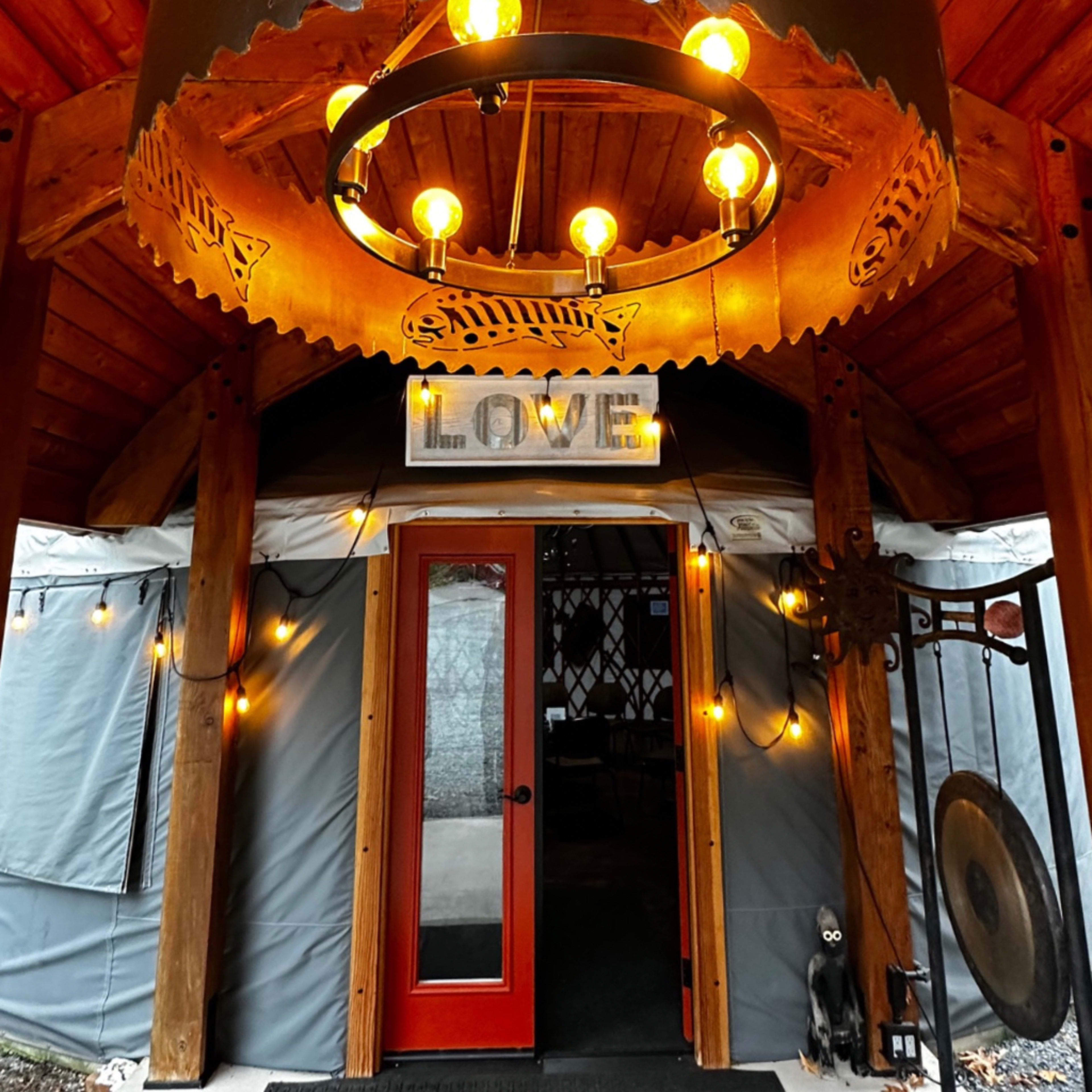 The entrance of a yurt adorned with a circular chandelier and string lights, featuring a red door and a sign that reads "LOVE."