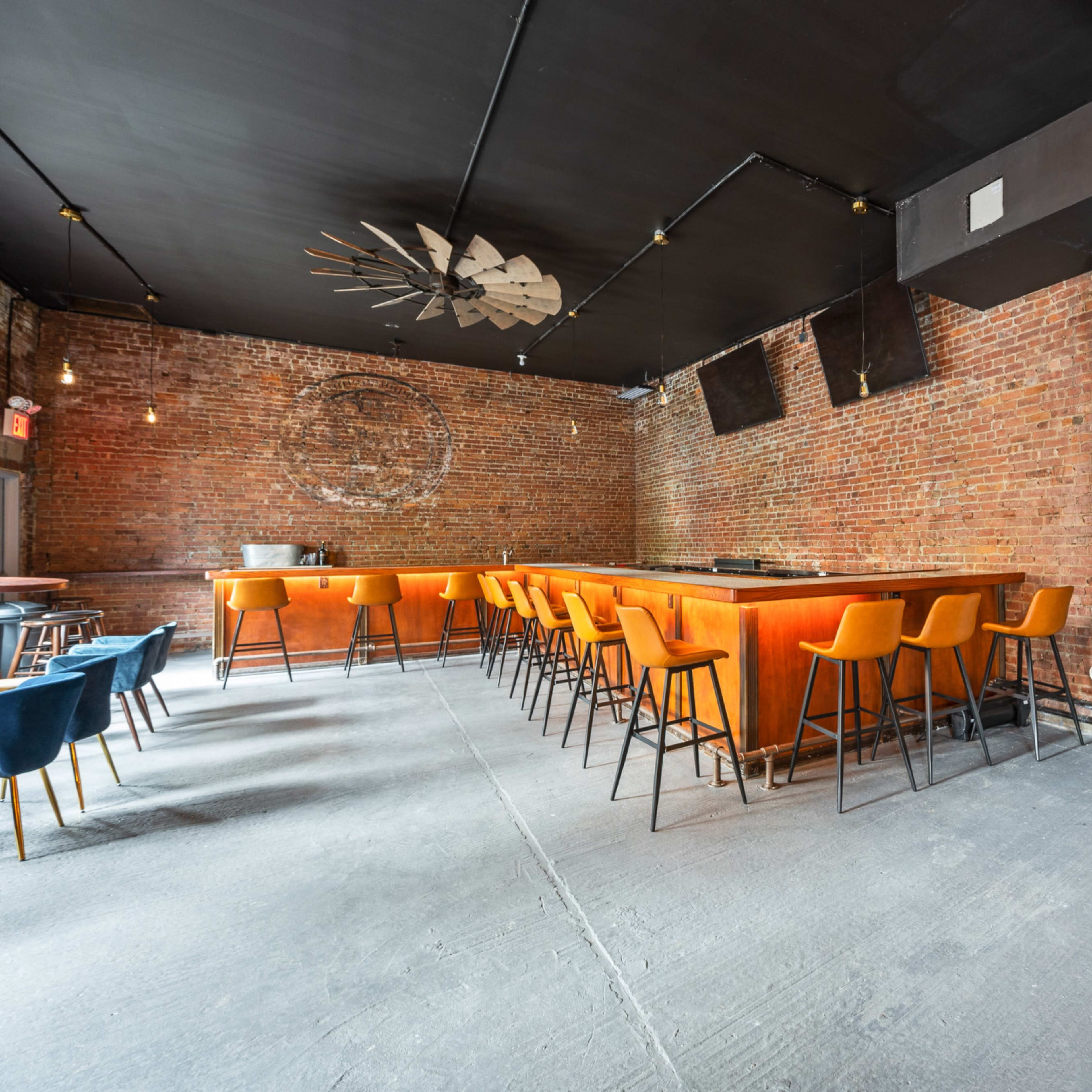 A spacious bar area with a wooden counter and orange stools, exposed brick walls, and a minimalist seating arrangement.