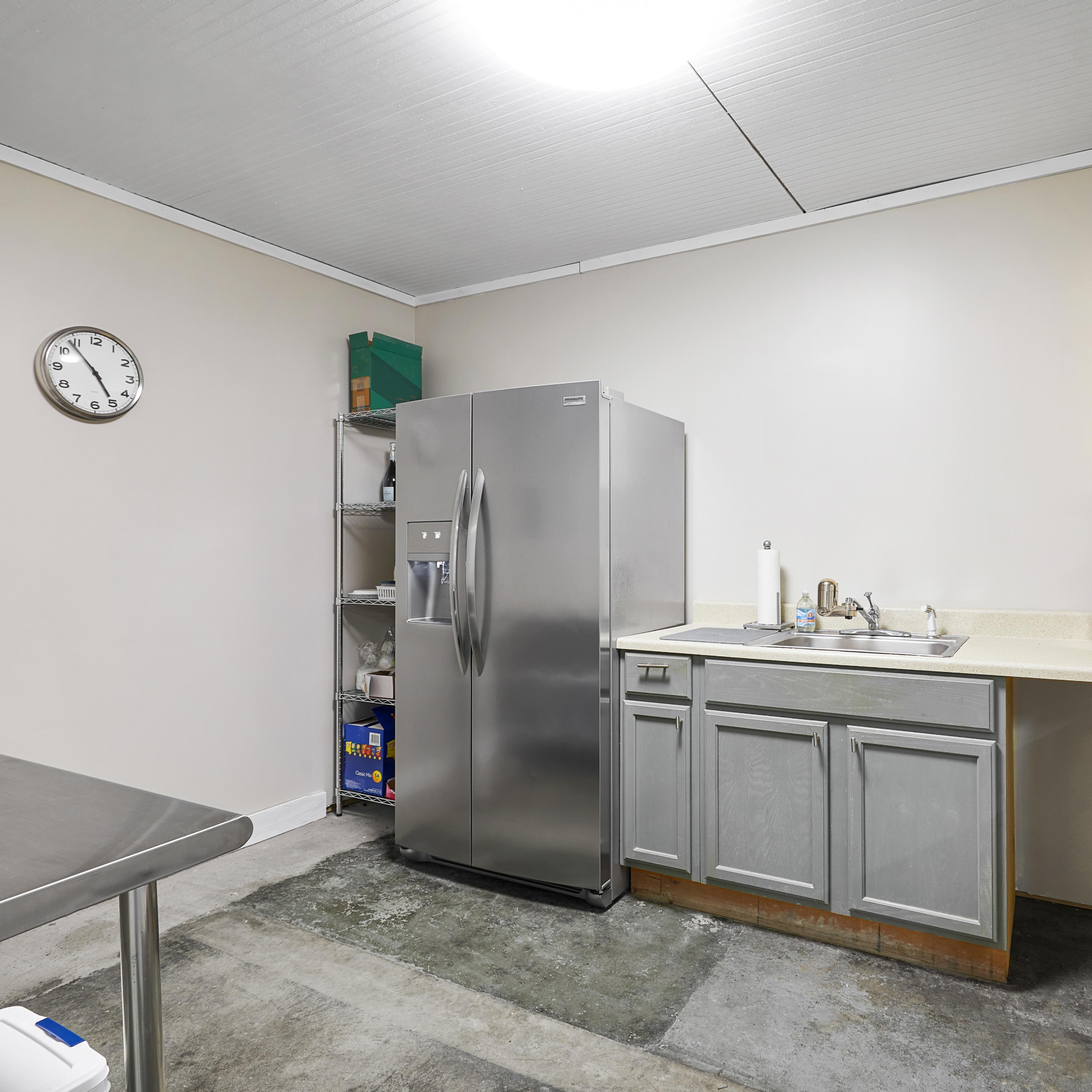A kitchen area with a stainless steel refrigerator, a microwave, a sink, and gray cabinets against light-colored walls.