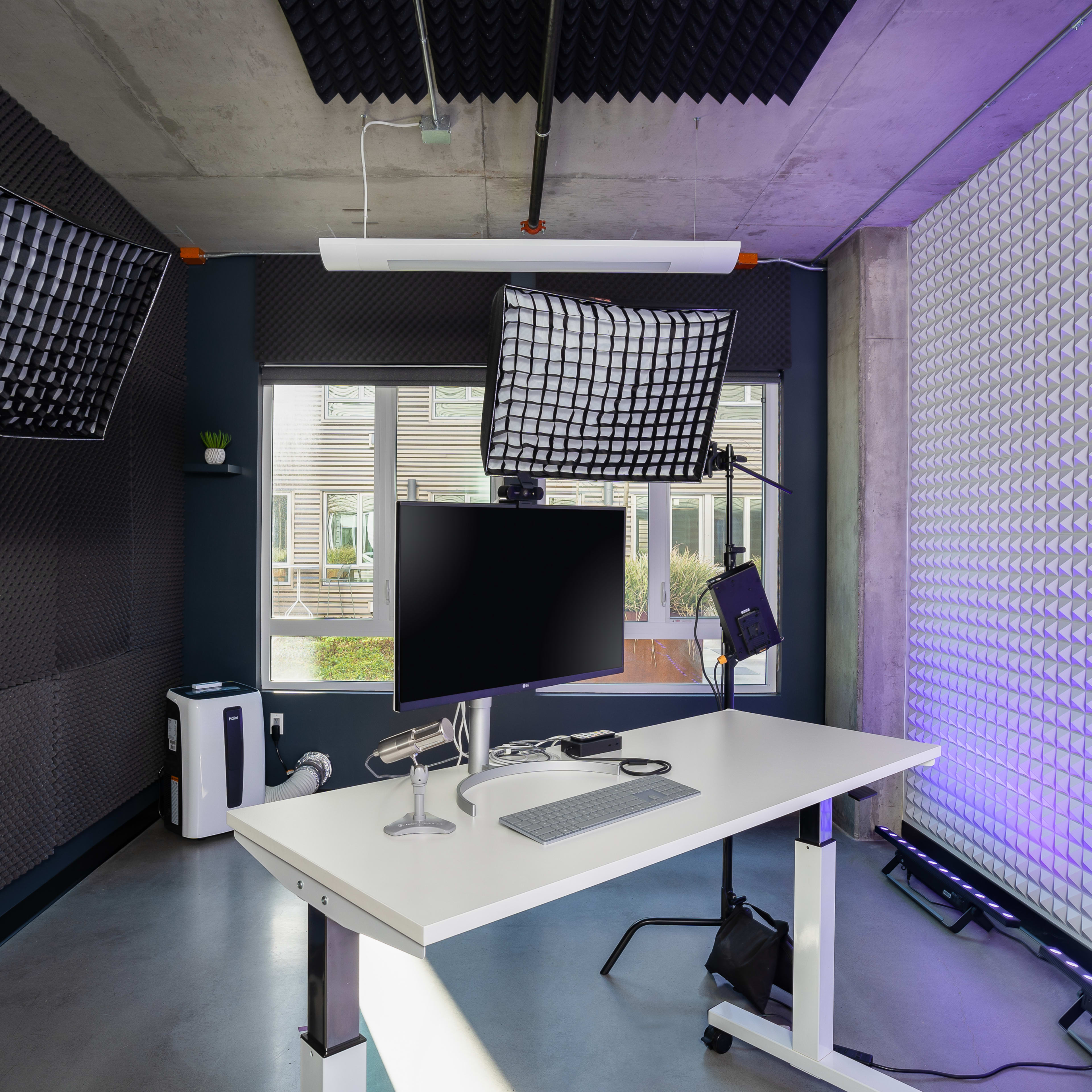 A modern office setup featuring a white desk with a monitor and keyboard, surrounded by sound-absorbing panels and studio lights.