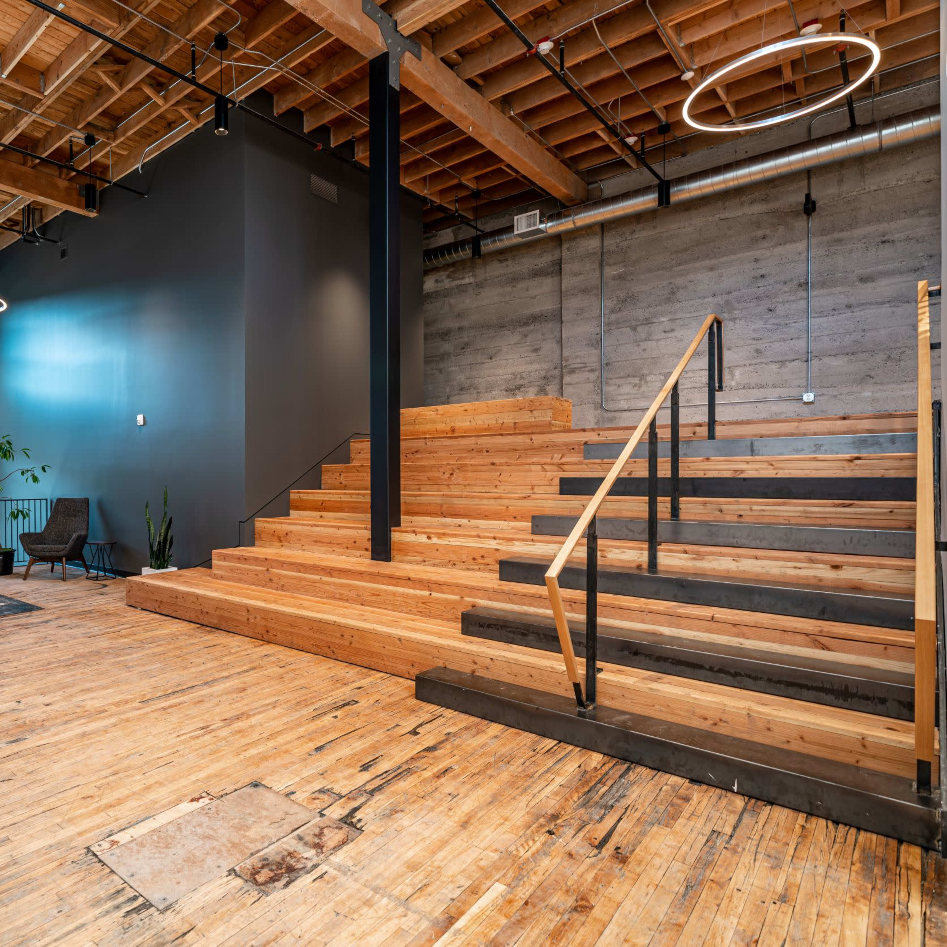 A spacious interior with wooden stairs leading to a raised area, featuring large windows and modern lighting fixtures.