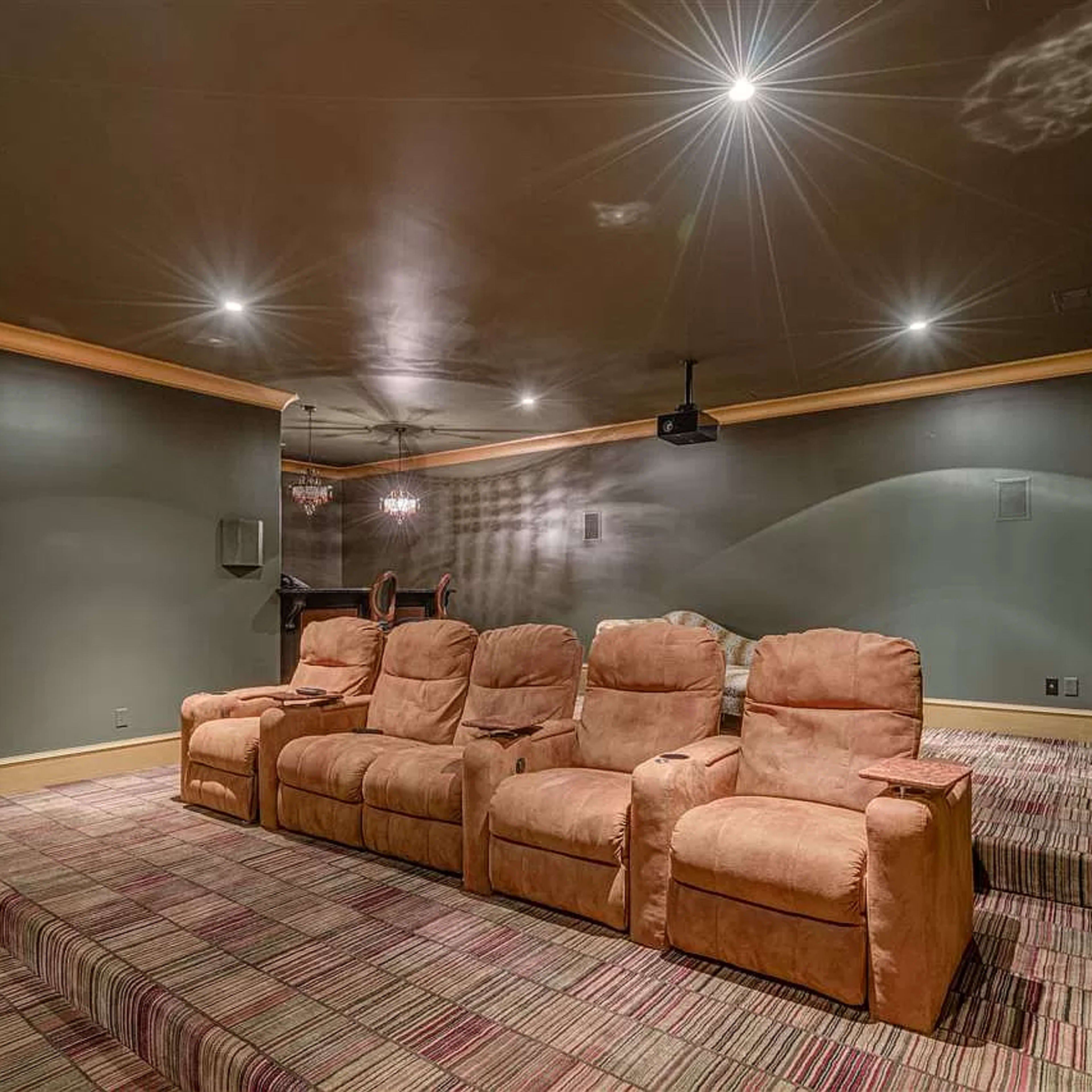 A home theater with a row of plush, brown recliners facing a blank wall, dimly lit by recessed ceiling lights.