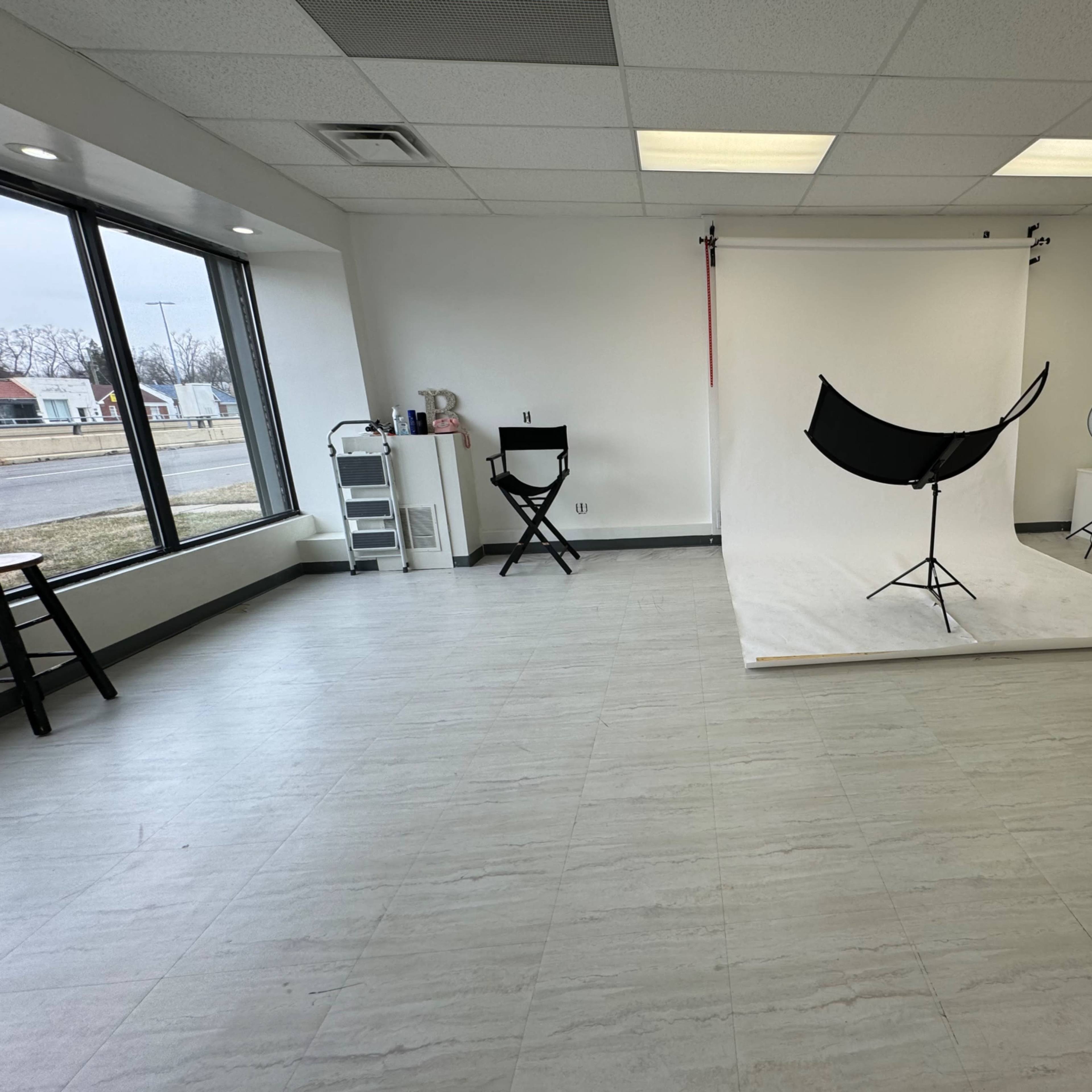 A photography studio with a white backdrop, multiple lighting setups, and empty seating areas.