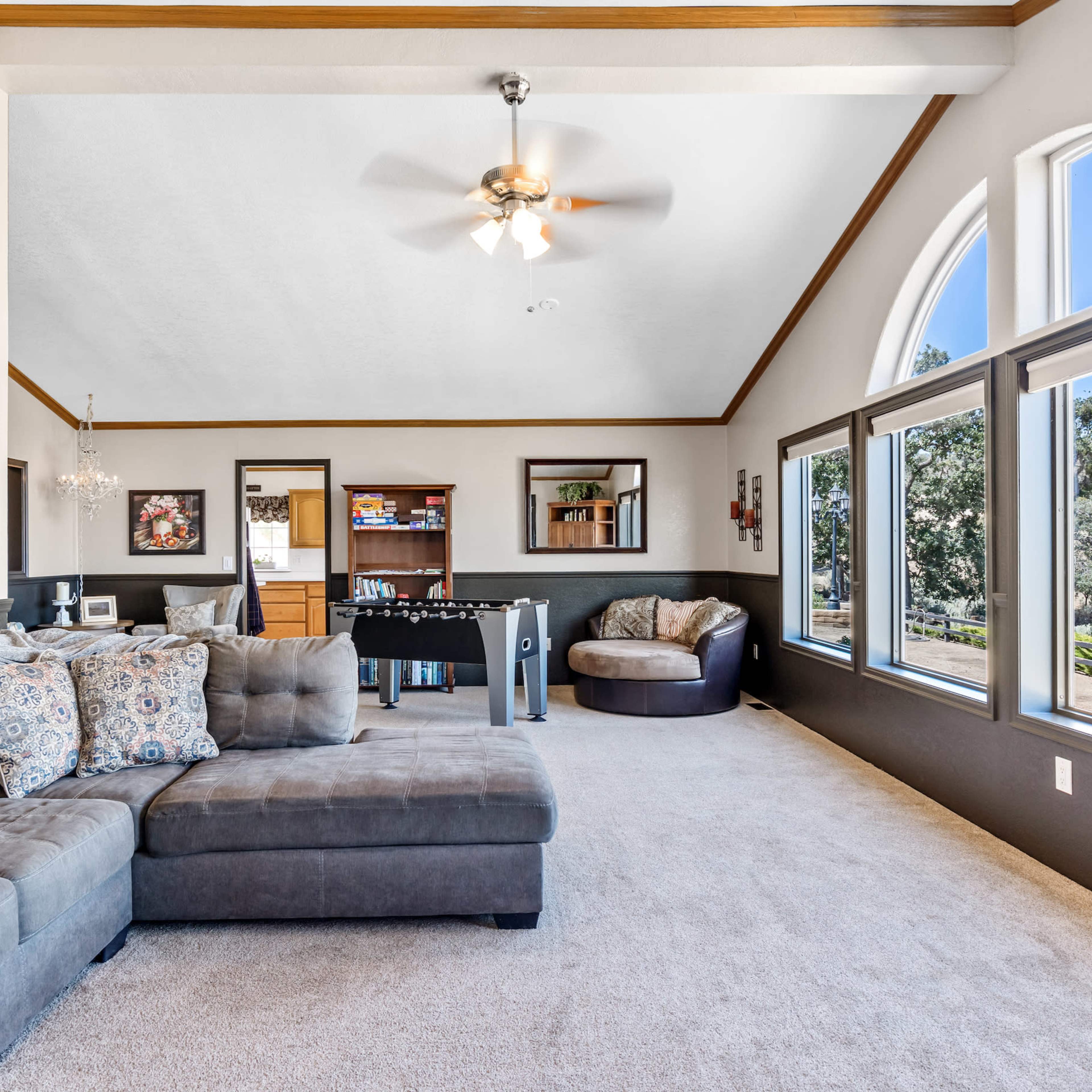 A spacious living room features a sectional sofa, a pool table, and large windows with a view of the outdoors.