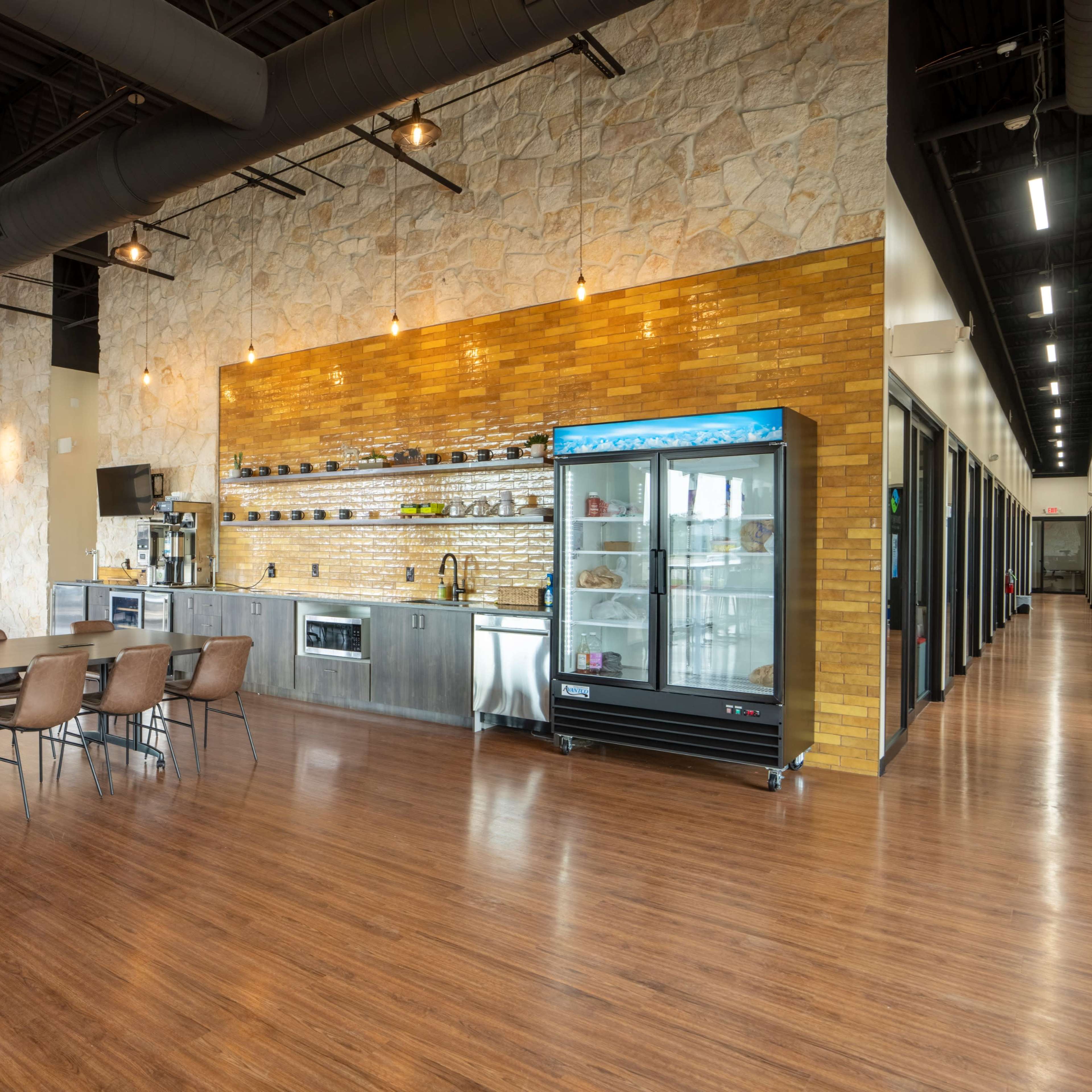 A spacious dining area with multiple tables, a stone accent wall, a equipped kitchen area, and a glass display refrigerator.