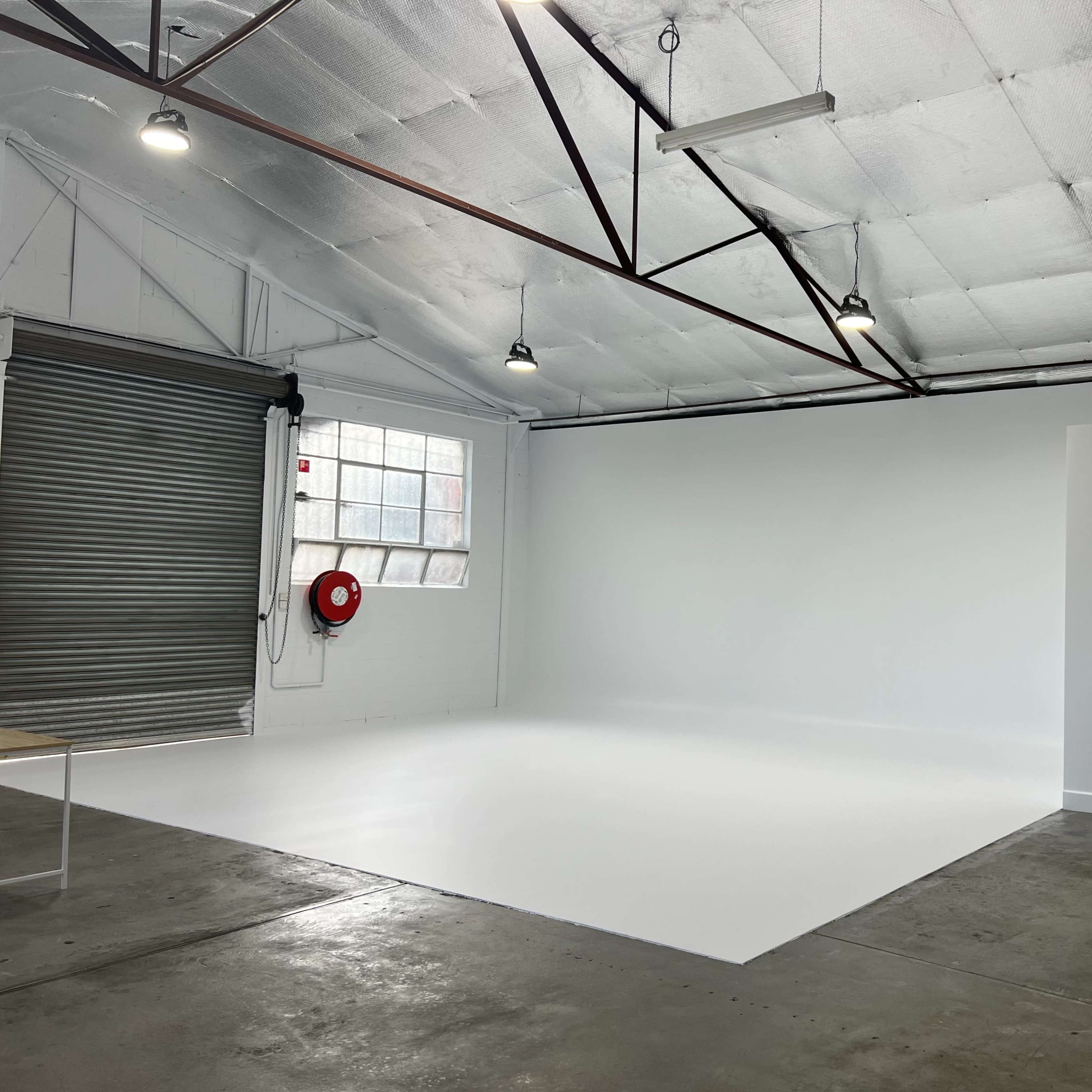 A spacious, well-lit studio with a white backdrop, large windows, and a gray curtain along one side.
