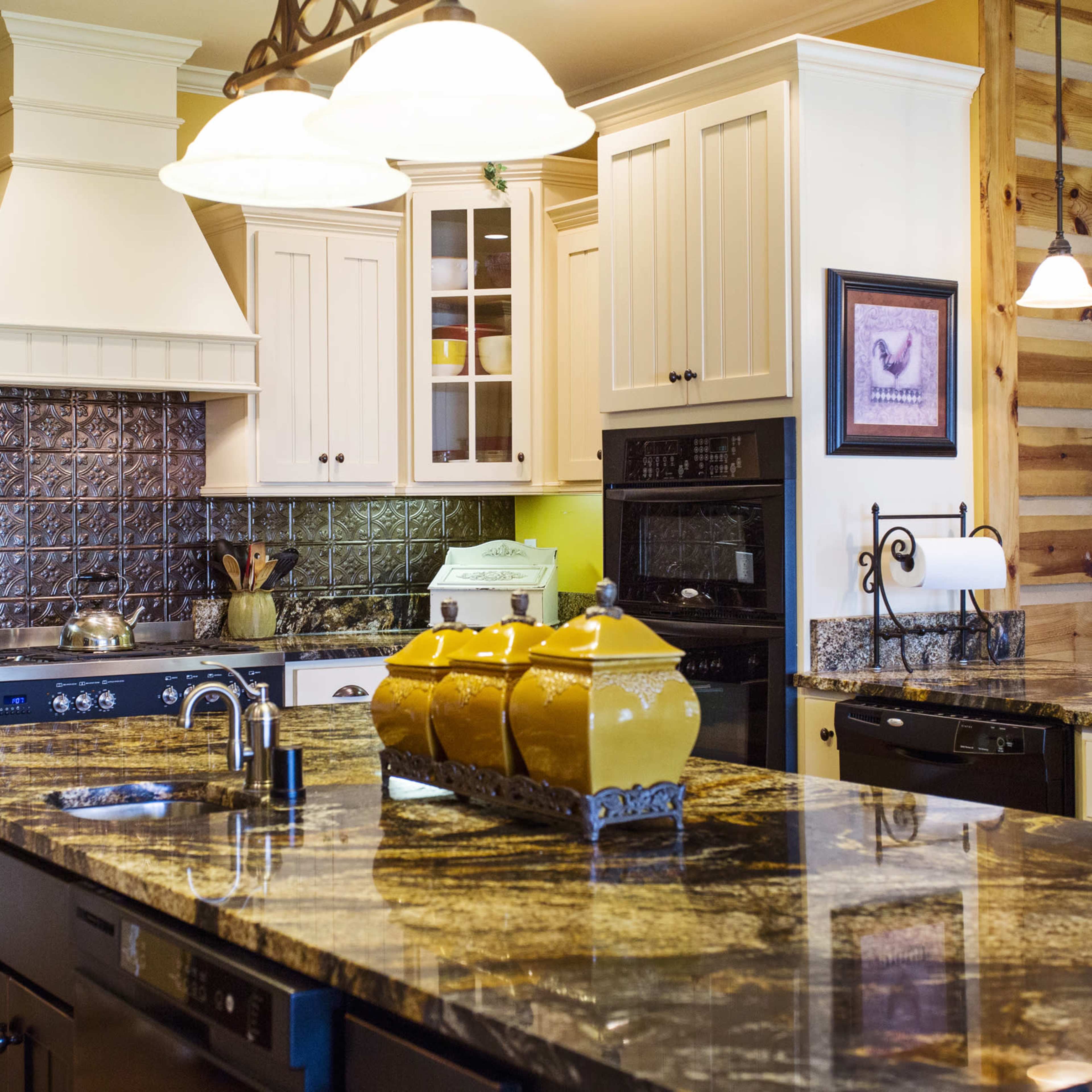 The kitchen features a granite island with a dark cabinet base, white cabinetry, stainless steel appliances, and pendant lighting above.