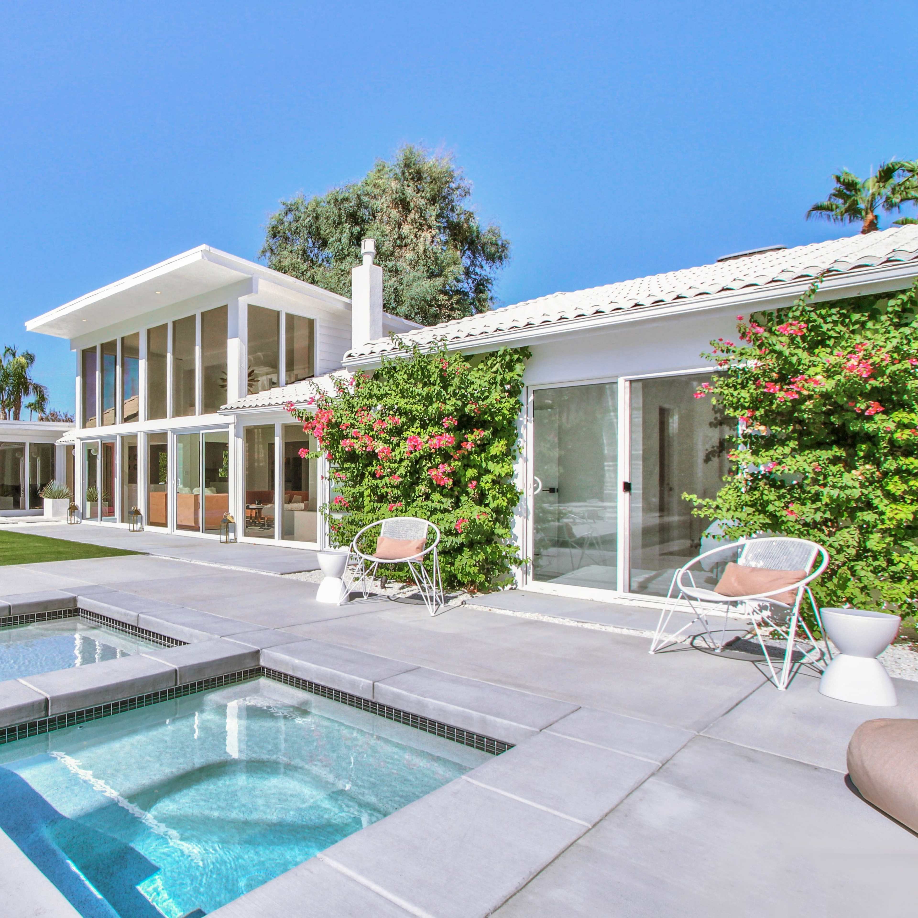 A modern house features a swimming pool and spa, surrounded by lush landscaping and bright blue skies.