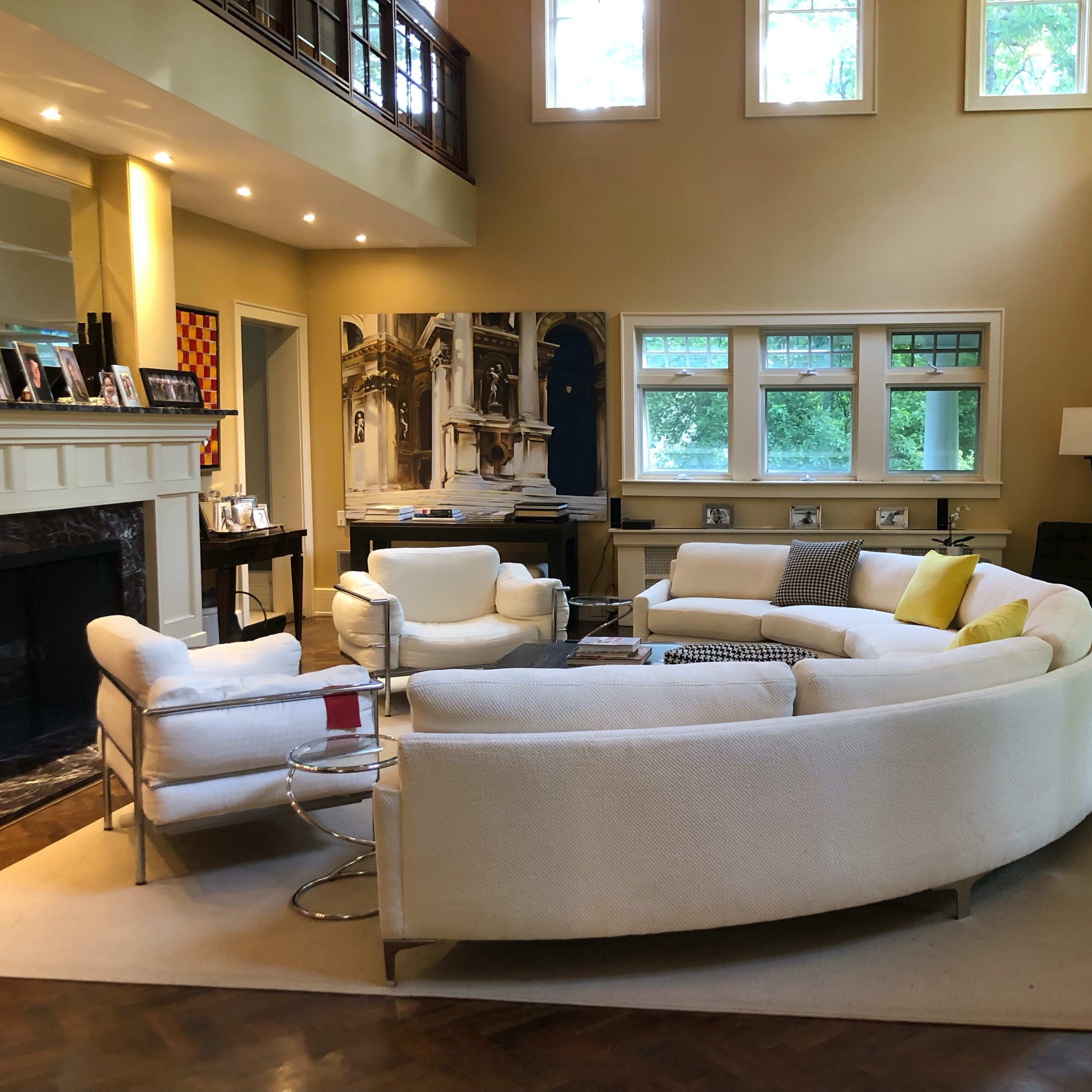 A spacious living room featuring a large, curved white sofa, two armchairs, and a coffee table, with large windows letting in natural light.