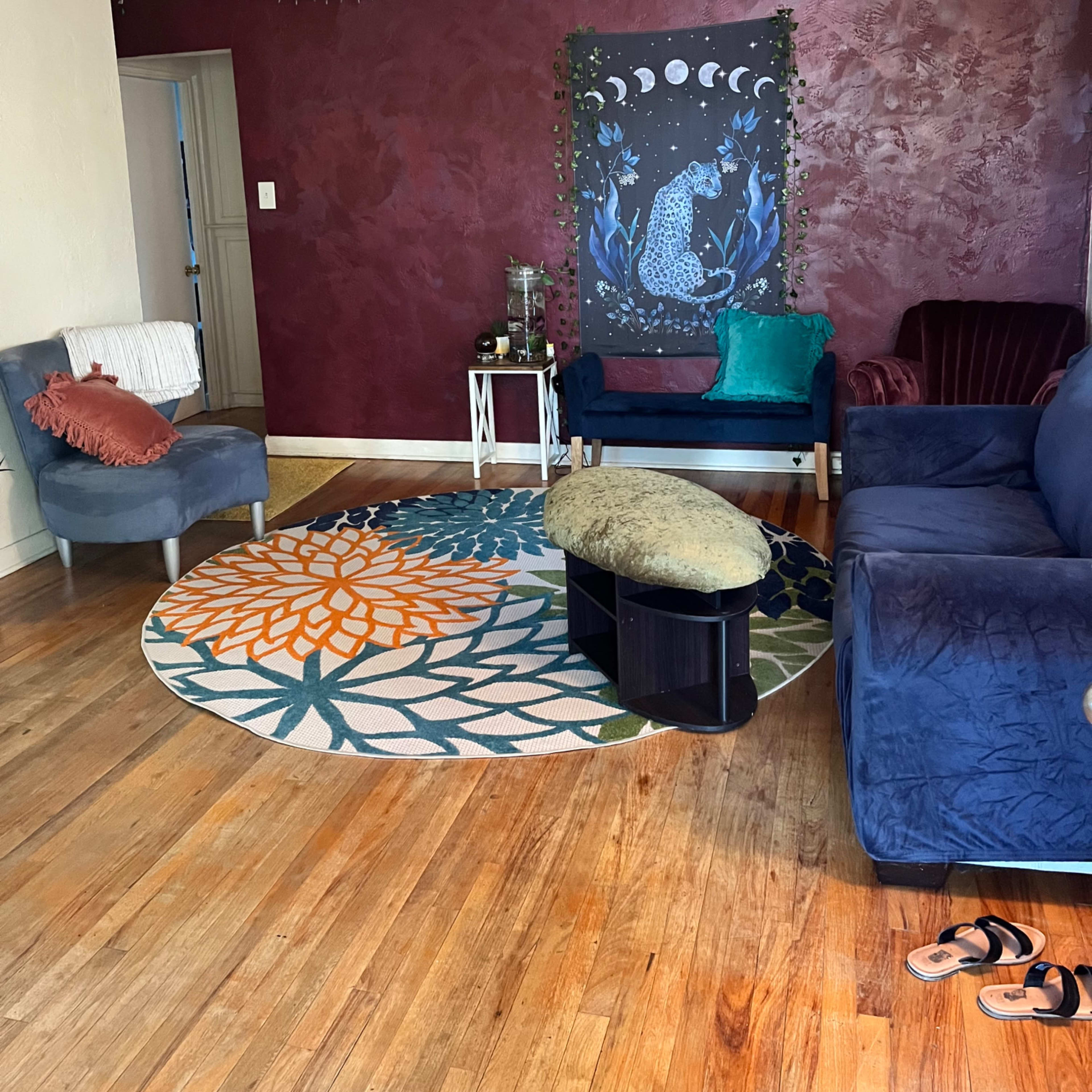 A living room with a maroon wall featuring a decorative mural, a round patterned rug, and various seating arrangements.